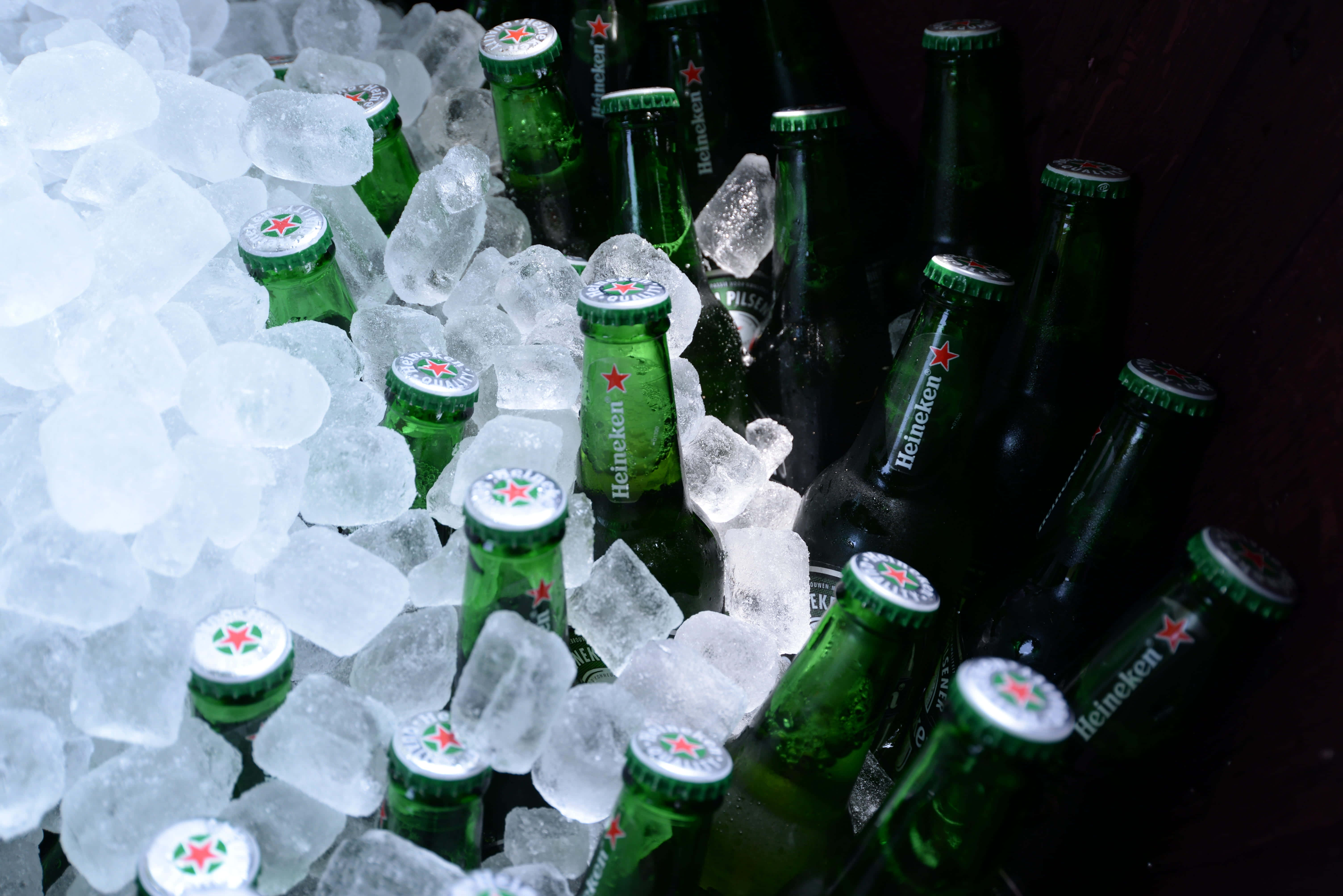 冷酷壁紙 壁紙 — 綠色喜力啤酒瓶在戲劇性燈光下，依偎在閃閃發光的冰塊中。