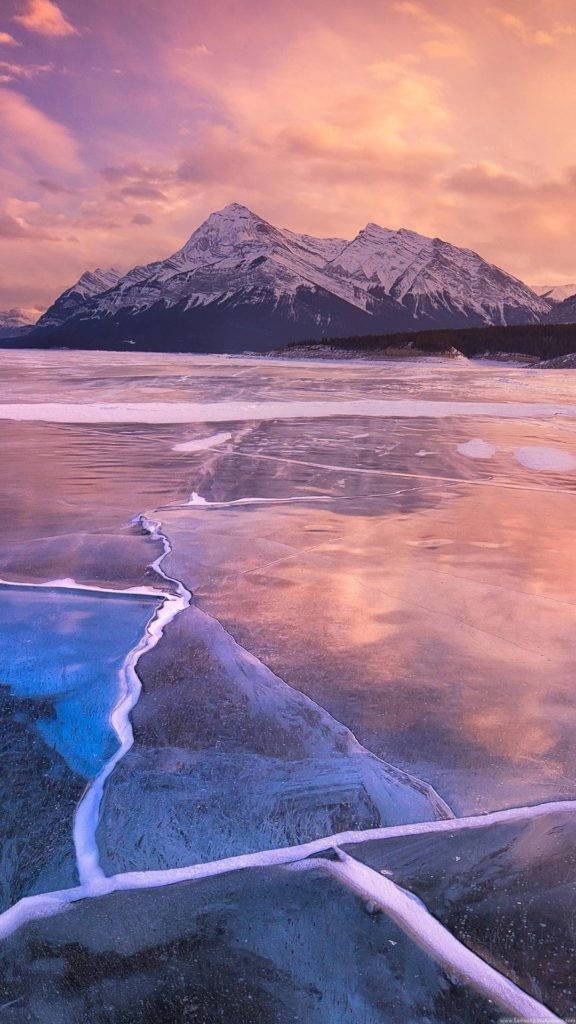 凍結海面自然 iPhone 背景 壁紙 — 冰凍的湖面反射出雪山上空充滿活力的粉紅色和橙色日落天空。