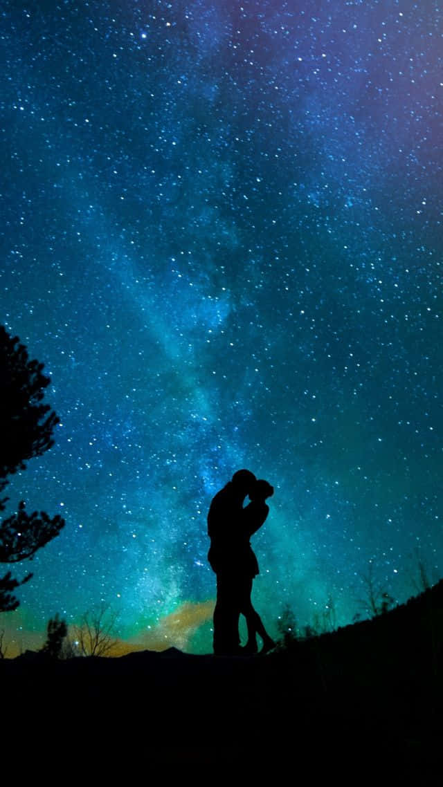 凝望繁星如海 壁紙 — 一對情侶在令人嘆為觀止的星空下擁抱的浪漫剪影，帶有充滿活力的藍色和藍綠色宇宙色調。