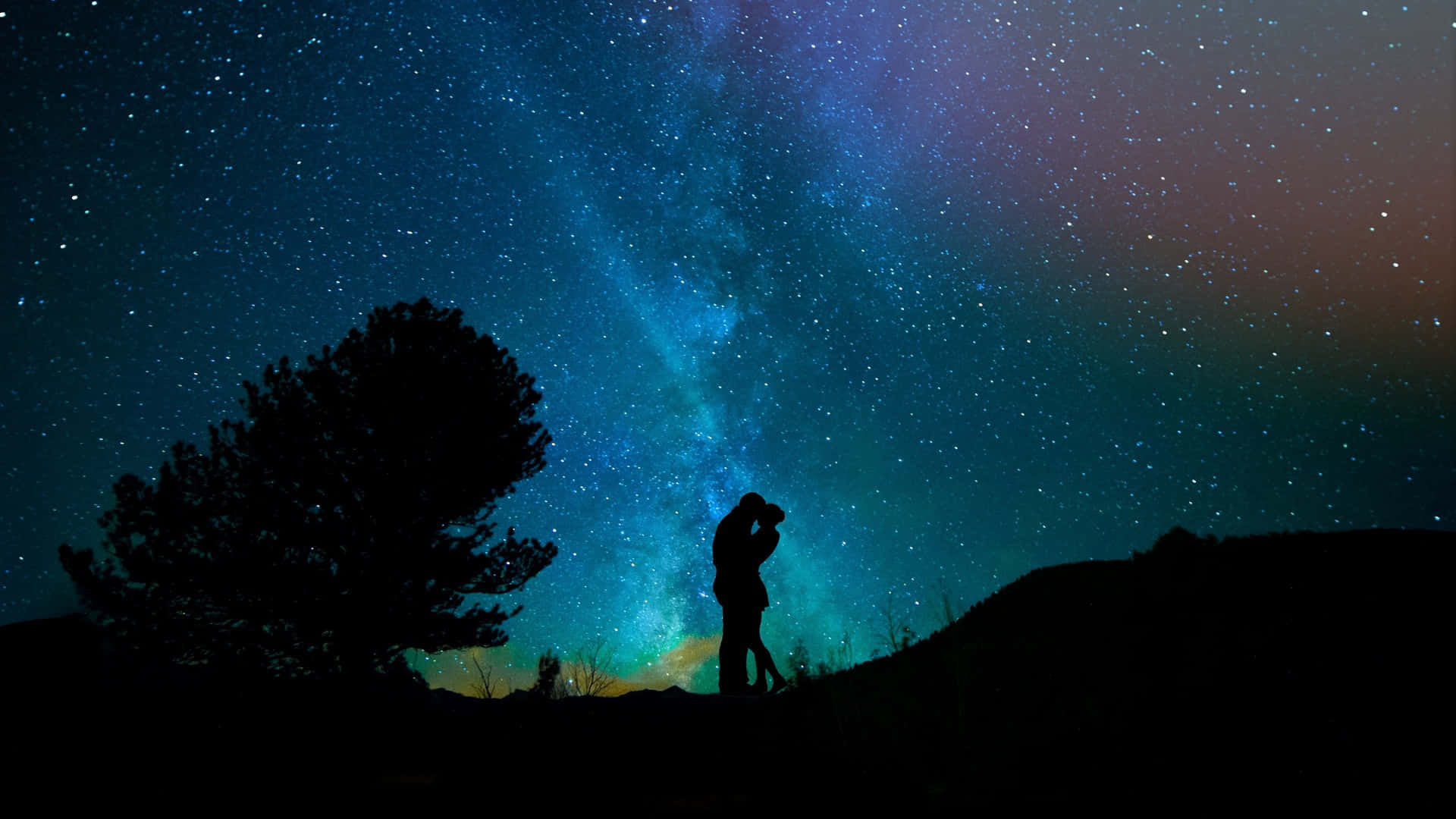凝視夜空的無限之美！ 壁紙 — 一對剪影情侶在充滿活力的星空下擁抱，銀河在一棵孤樹上方閃耀。