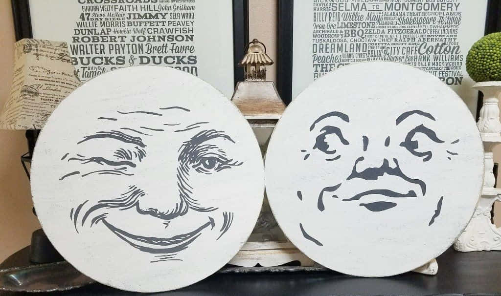 凝視月亮面容的驚豔之美 壁紙 — 兩個白色圓形牌匾，帶有黑色線條藝術，描繪微笑的月亮臉，放在一個深色架子上，旁邊是復古裝飾。