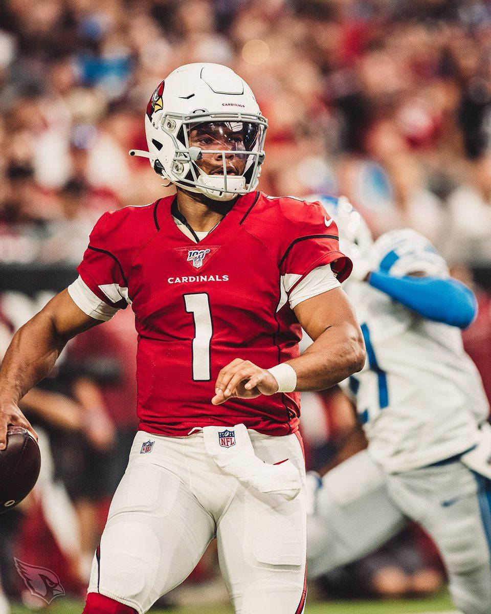 凱勒·默里對戰底特律獵鷹隊 壁紙 — 一位專注的NFL四分衛，身穿紅色紅雀隊一號球衣，在體育場燈光下準備在比賽中擲出橄欖球。