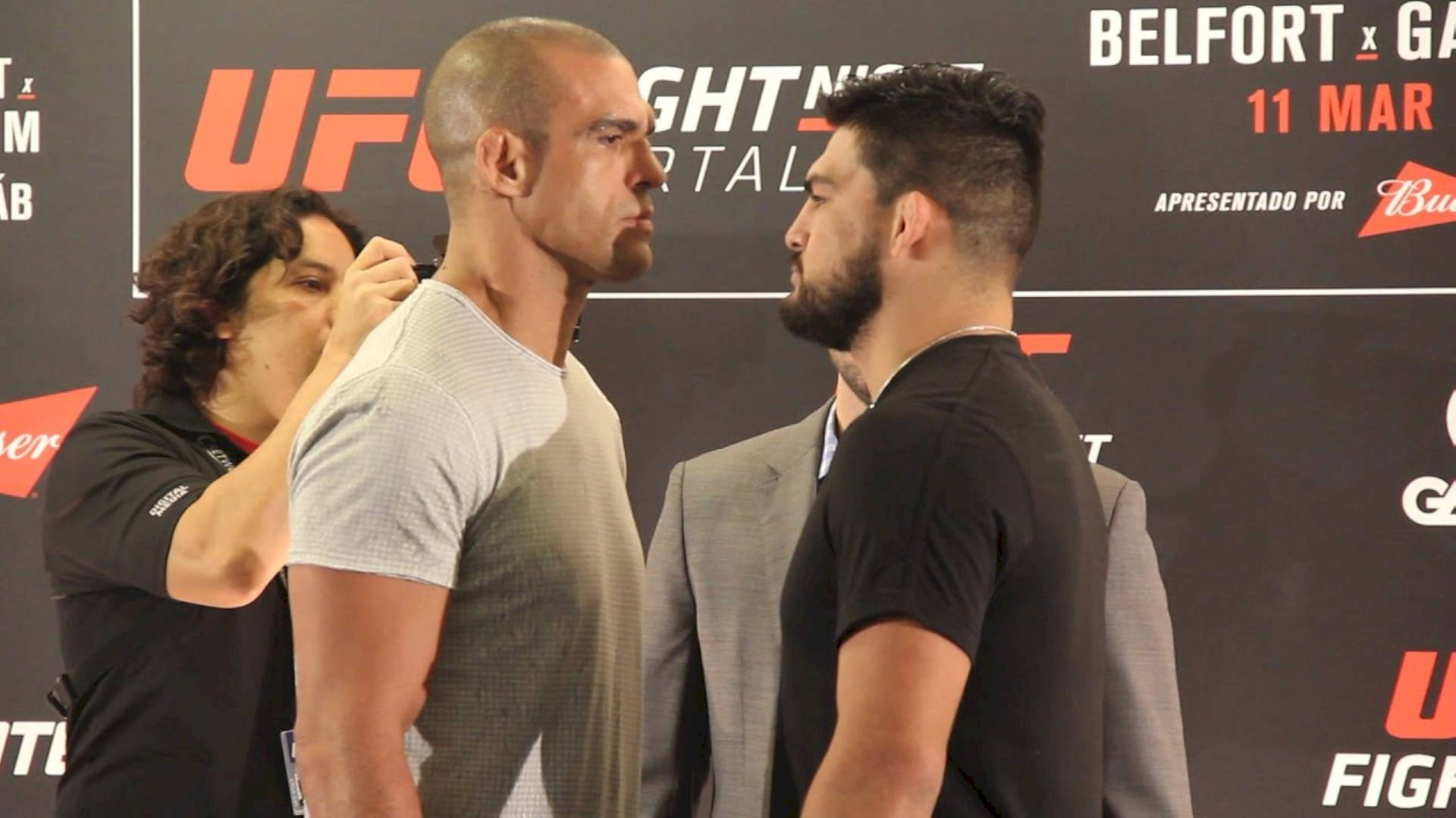 兩名男性UFC拳手在稱重活動中面對面站立，裁判調整其中一人的襯衫。