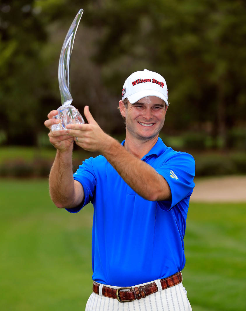 凱文·斯特雷爾曼舉起獎盃 壁紙 — 一位身穿藍色襯衫、面帶微笑的高爾夫球手，在綠色球場上自豪地高舉水晶獎盃並豎起大拇指。