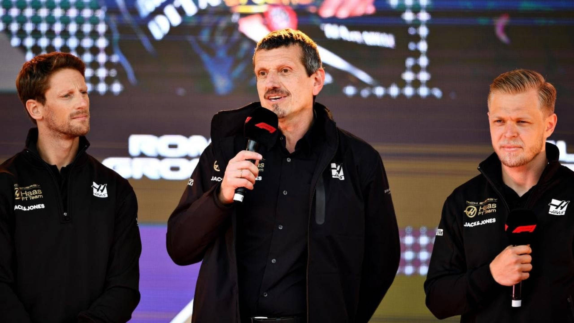 三名身穿黑色外套的F1車隊成員在記者會上使用咪高峰。