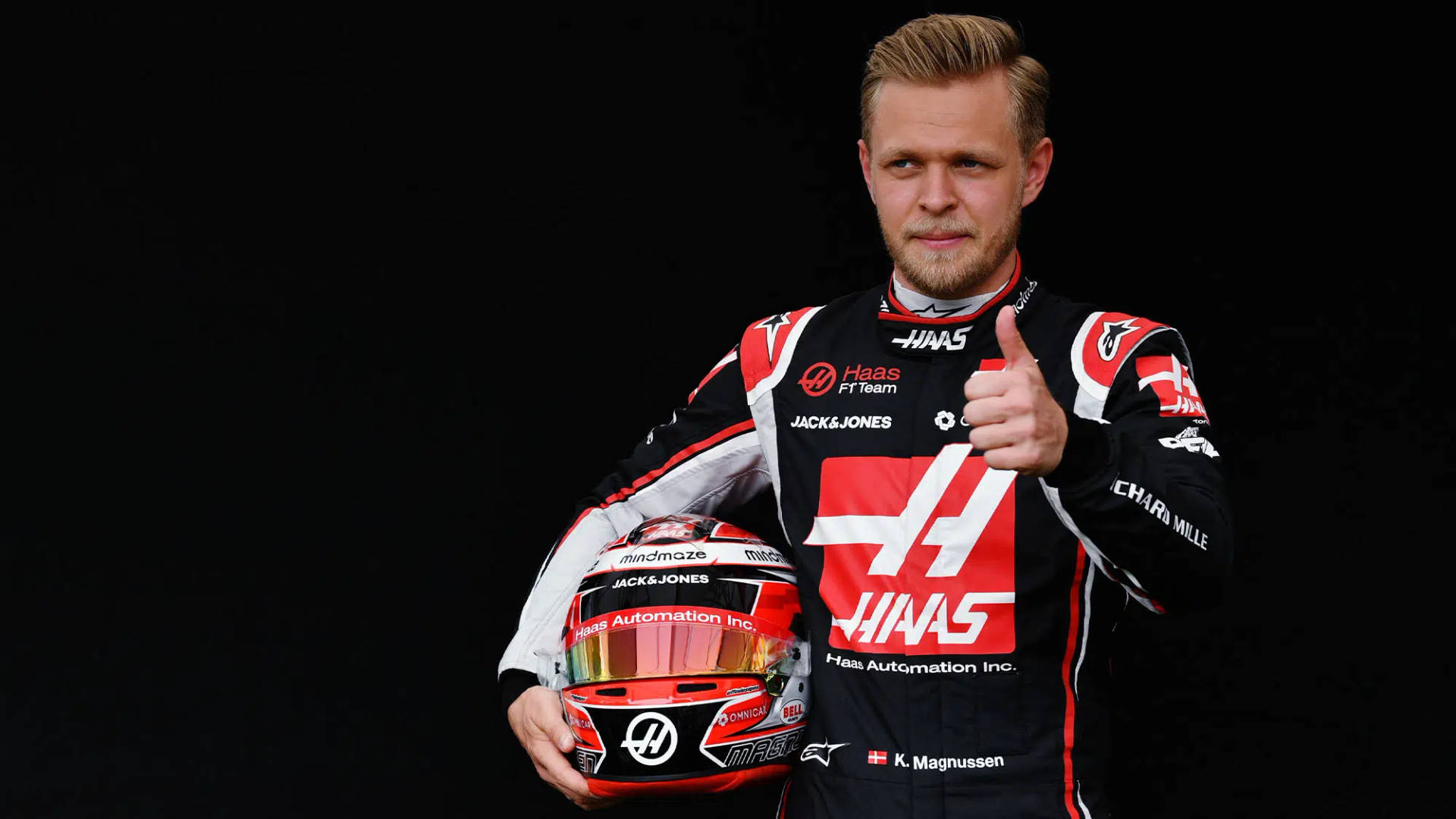 F1車手奇雲·麥奴臣身穿哈斯制服手持頭盔豎起大拇指。