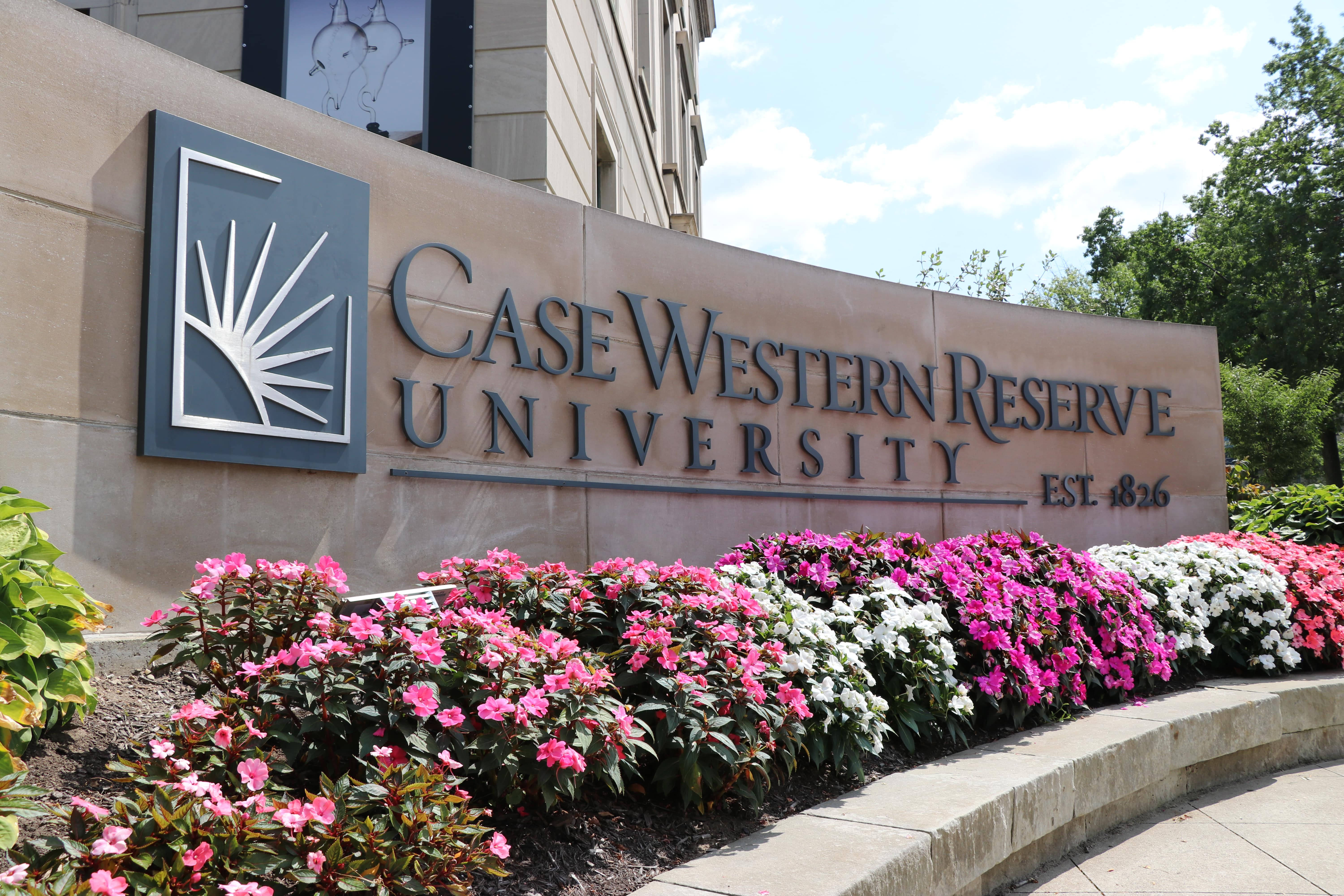 凱斯西儲大學校門 壁紙 — Case Western Reserve University 標誌，前方有粉紅色和白色花朵，背景是明亮的藍天。