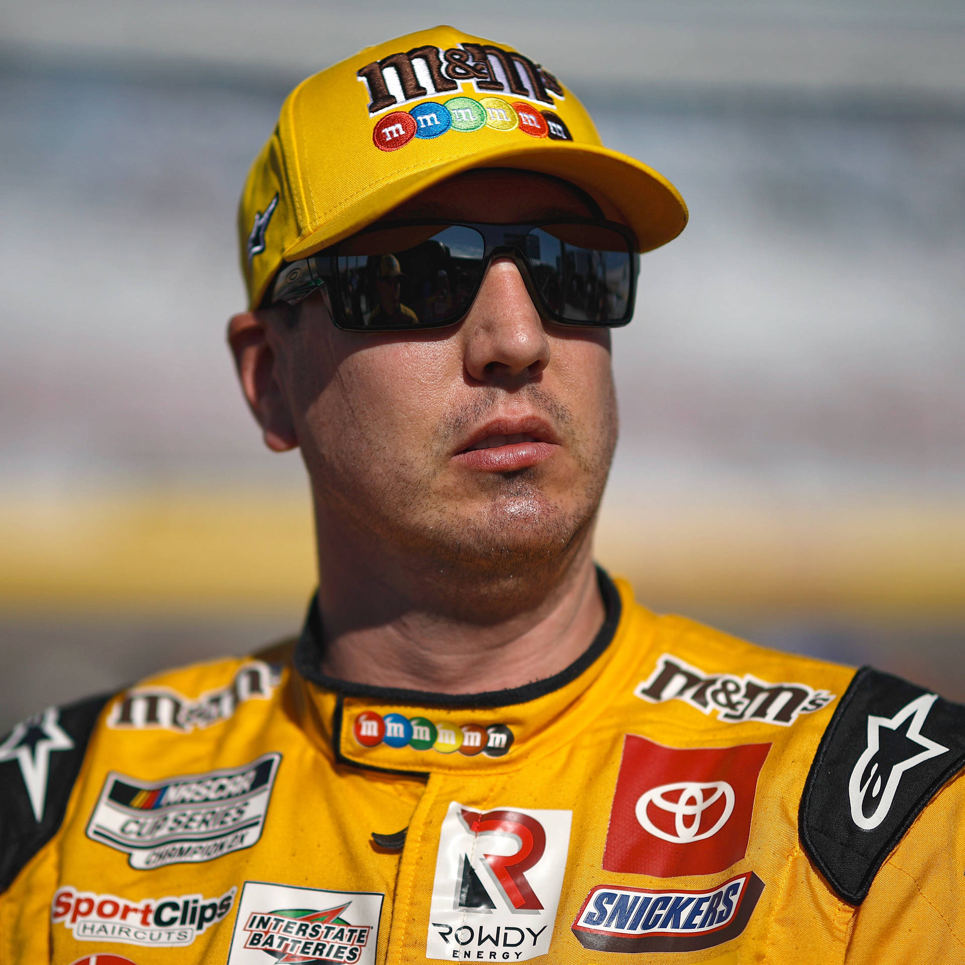 NASCAR車手身穿黃色M&M's賽車裝備，戴著太陽眼鏡在賽道上。