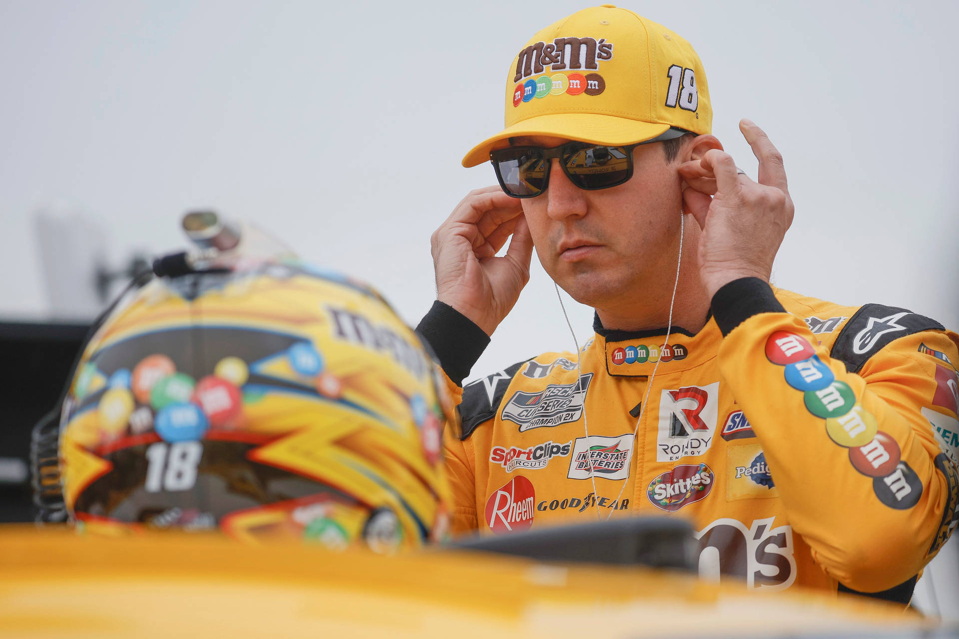 身穿黃色M&M's制服的NASCAR車手在頭盔附近調整耳機。