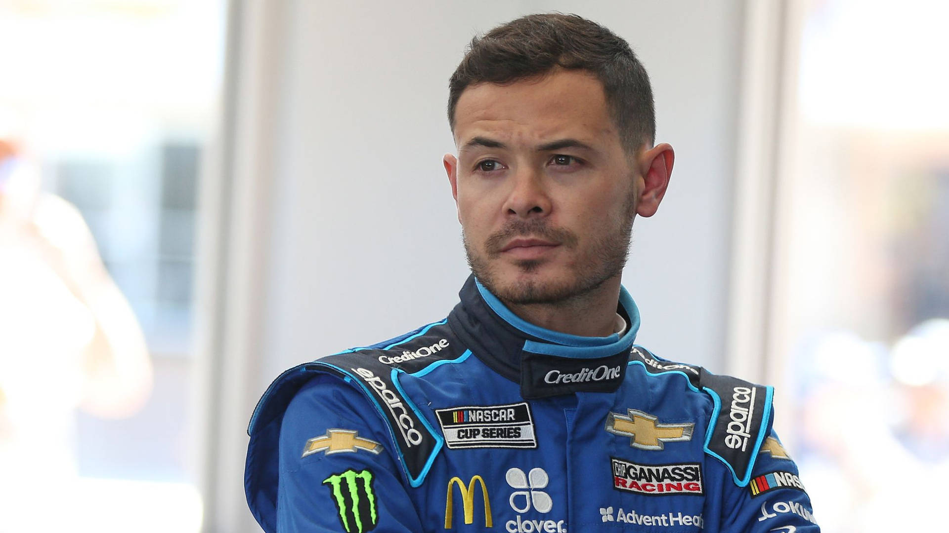 身穿藍色賽車服帶有贊助商標誌的NASCAR車手在室內表情嚴肅。