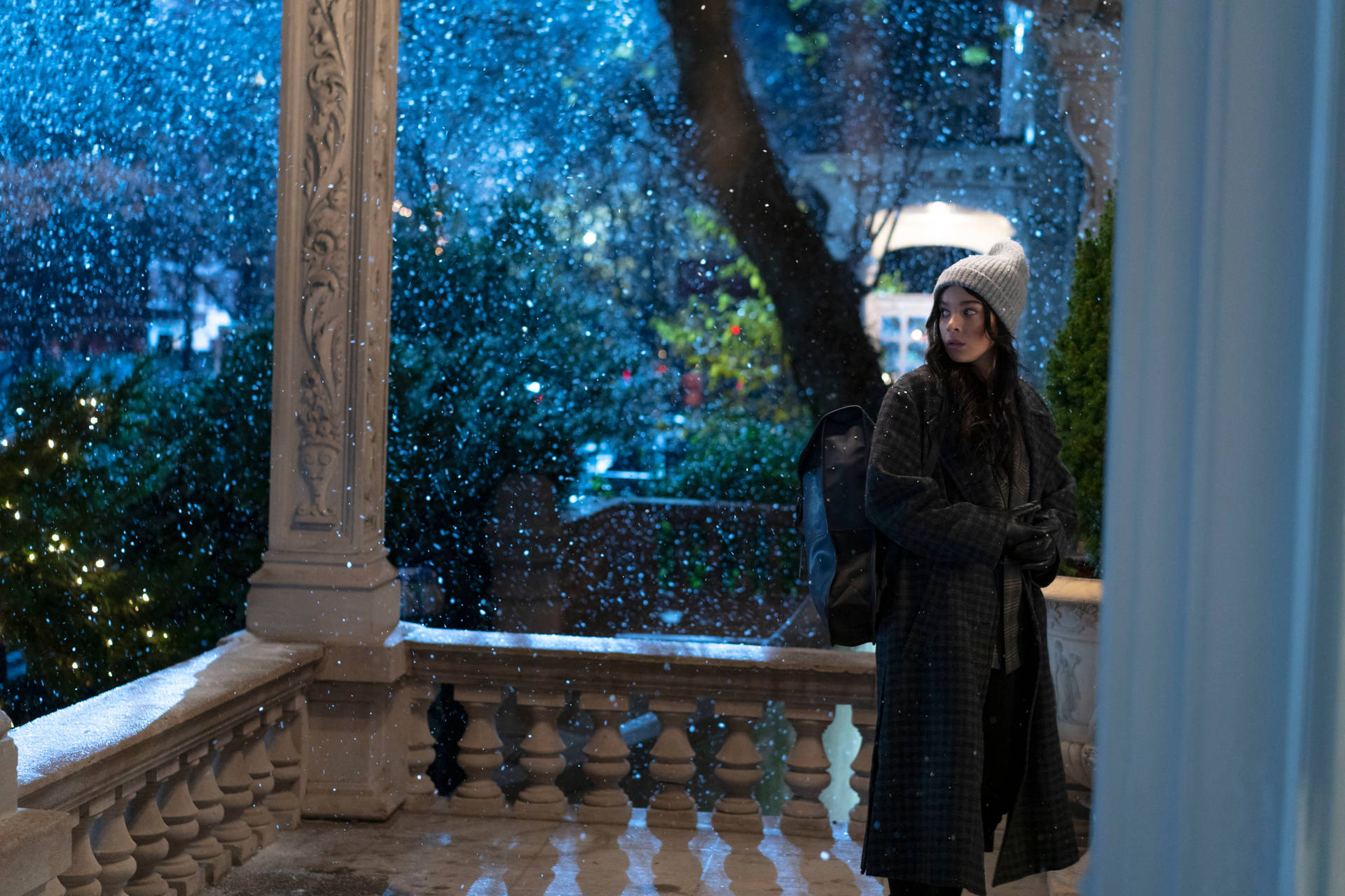 穿著冬季外套和帽子的女性在夜間降雪時站在積雪的門廊上。
