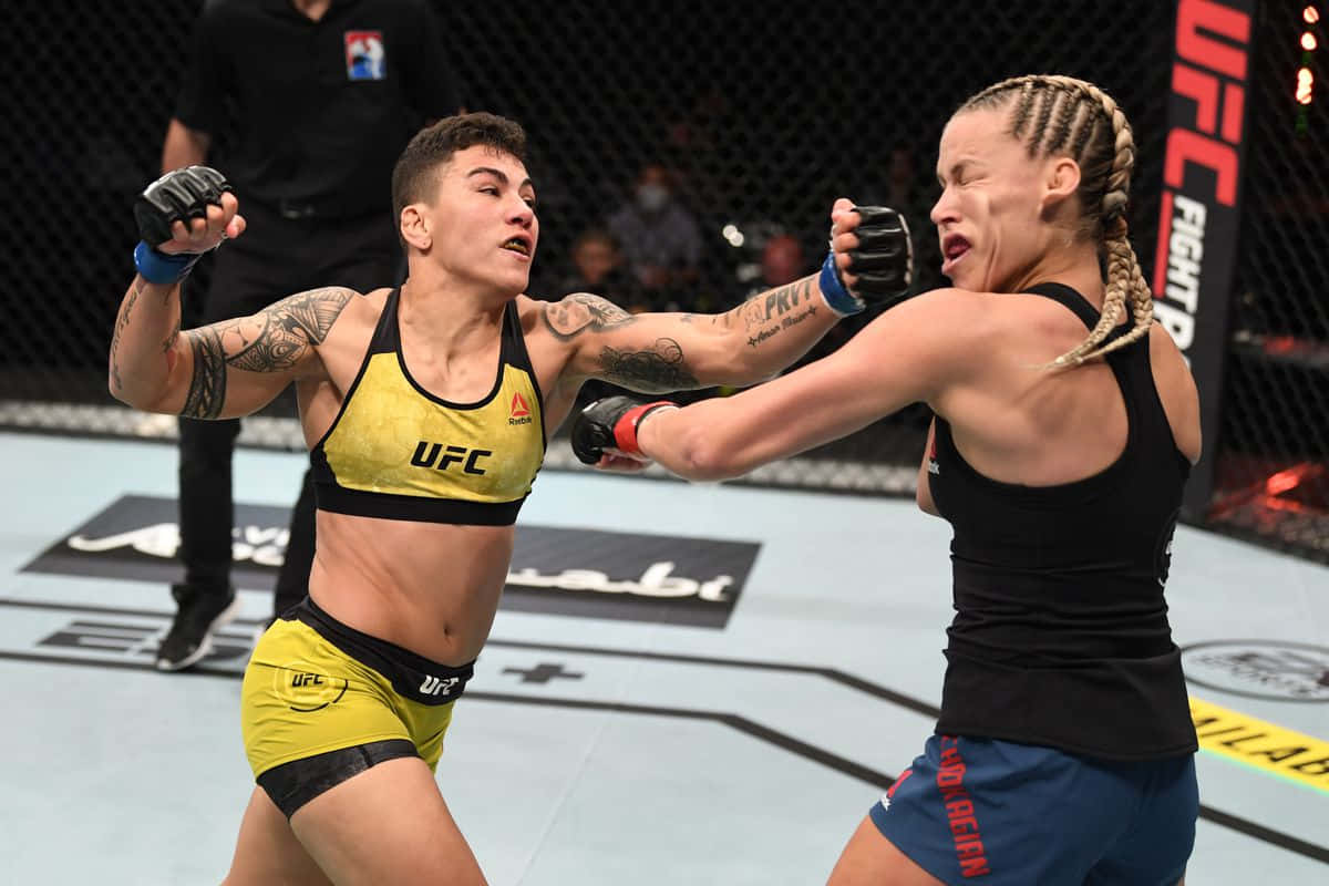 凱特琳·丘卡吉安被對手擊中面部 壁紙 — 兩名女性MMA拳手在激烈的UFC八角籠比賽中交鋒，身上有紋身，表情專注。
