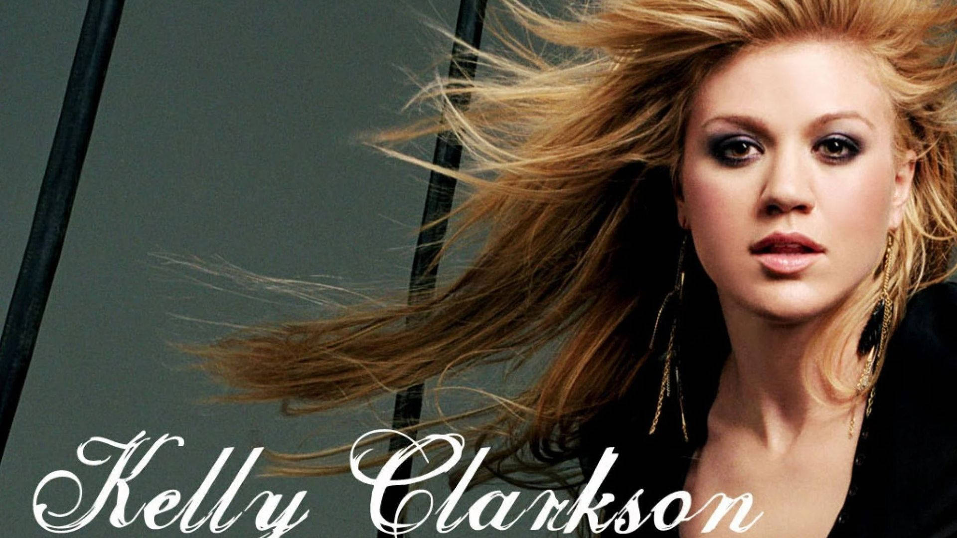 凱莉·克蘭森迷人風采 壁紙 — Kelly Clarkson 一頭被風吹拂的金髮和煙燻眼妝，在深灰色背景下強烈凝視。