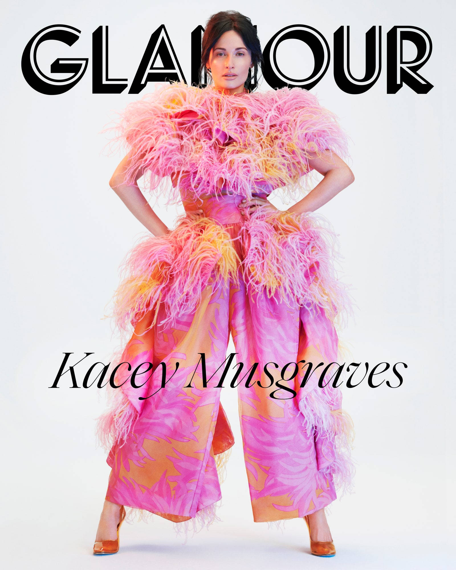 凱西·穆斯格雷夫斯時尚寫真 壁紙 — Kacey Musgraves 自信地擺姿勢，身穿鮮豔的粉紅色和橙色羽毛長袍，背景是純白色。