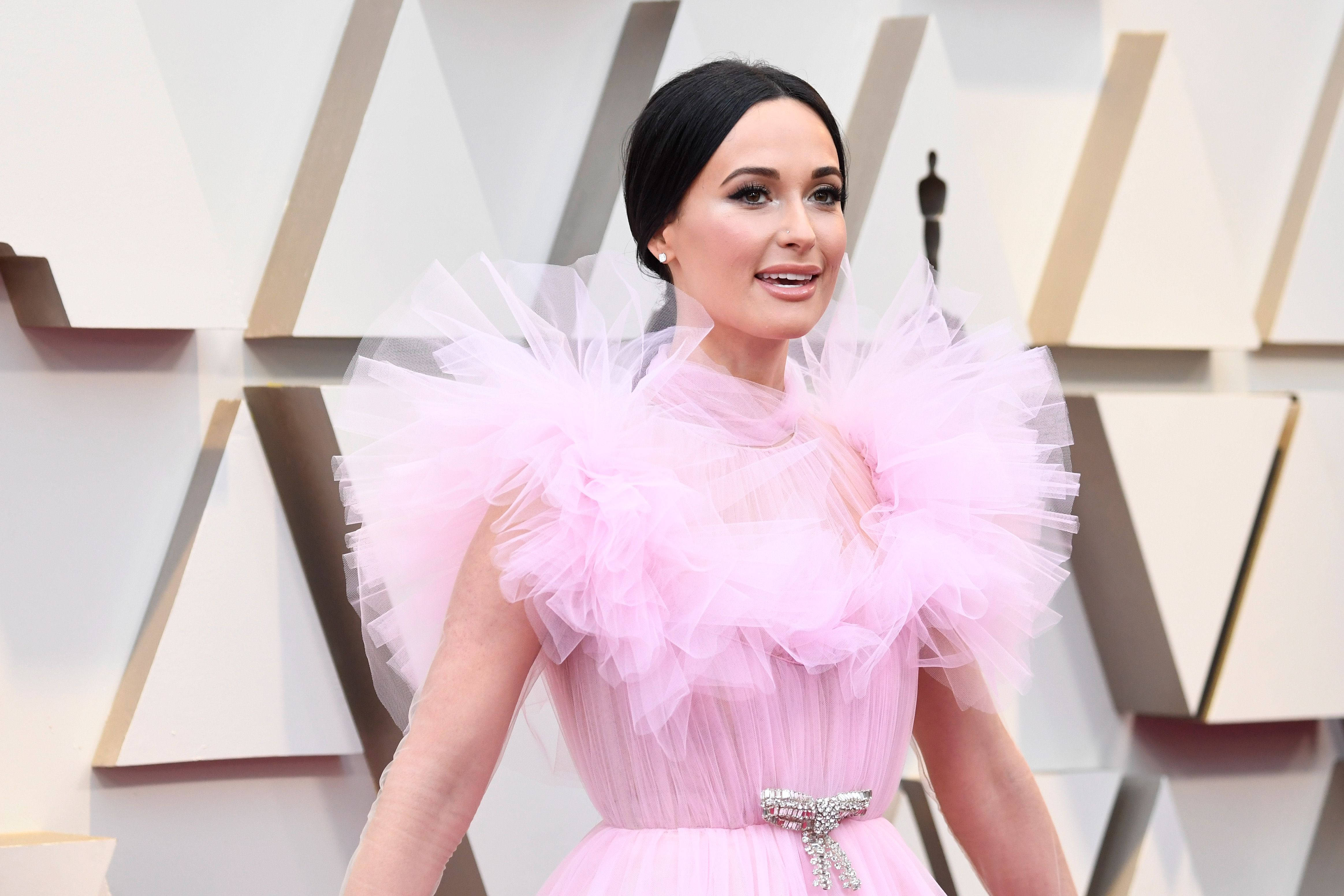 凱西·穆斯格雷夫斯穿粉紅禮服 壁紙 — Katy Perry 在奧斯卡紅地毯上穿著蓬鬆的粉紅色薄紗禮服微笑，背景為幾何圖案。