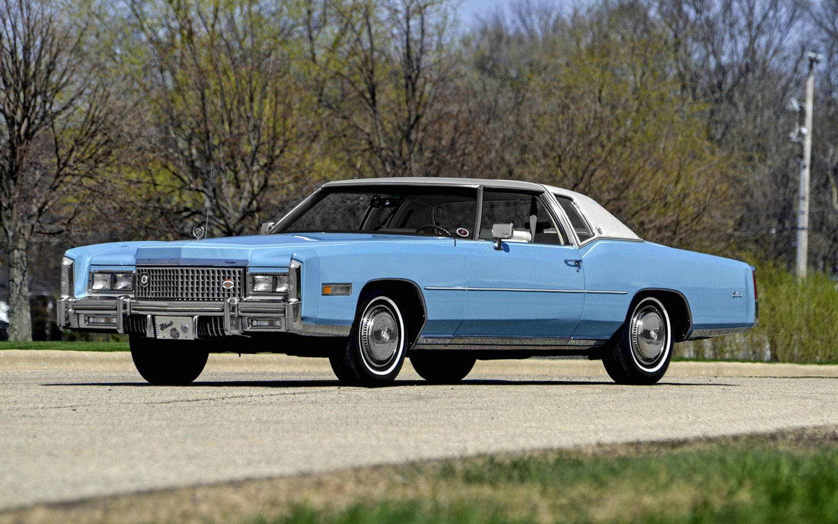 淺藍色經典凱迪拉克 Coupe DeVille 白色車頂，停在碎石路上，附近有樹木。