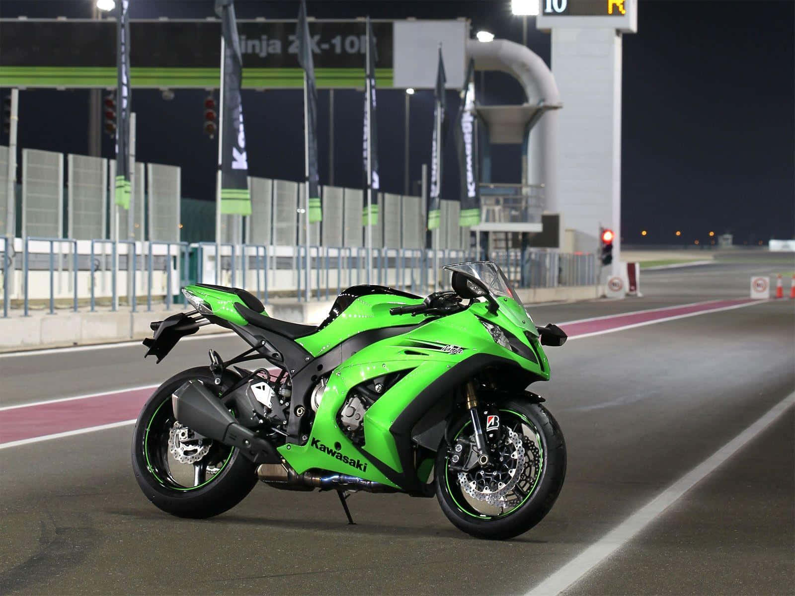 出色的川崎Ninja ZX10R機車背景 壁紙 — 一架鮮綠色嘅Kawasaki Ninja ZX-10R電單車喺夜晚停喺賽車場上，喺明亮嘅人造燈光下。
