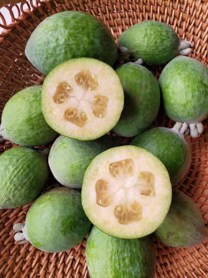 切半的 Feijoa（菠蘿番石榴） 壁紙 — 新鮮的綠色菲油果，果肉多汁，放在編織籃中，展示其星形種子和紋理表皮。
