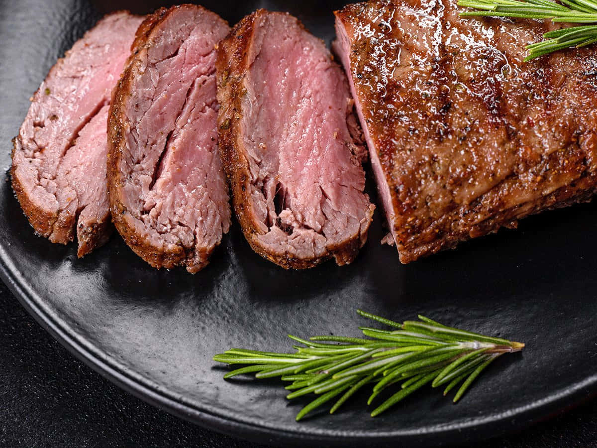 meat 桌布 壁紙 — 切片五成熟牛肉配迷迭香裝飾，置於磨砂黑色餐盤上。