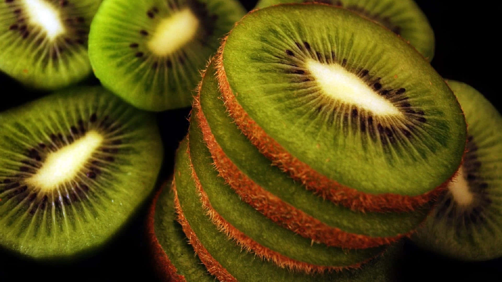 Kiwi 桌布 壁紙 — 切片奇異果在深色背景下展現出鮮綠色果肉和絨毛狀棕色外皮。
