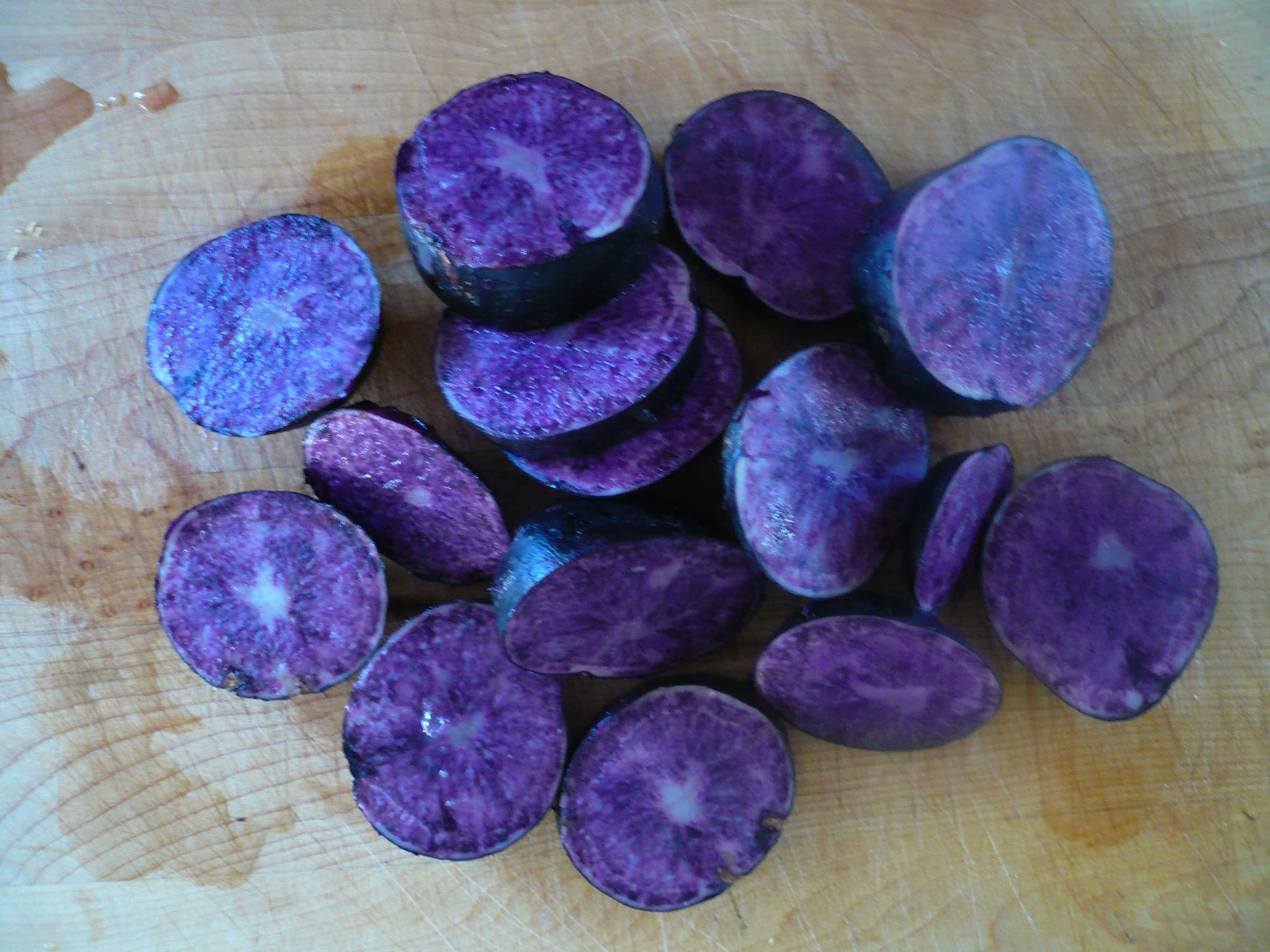 Purple Potato 桌布 壁紙 — 切片紫薯帶有鮮豔的內部，放在一個使用已久的木製砧板上。