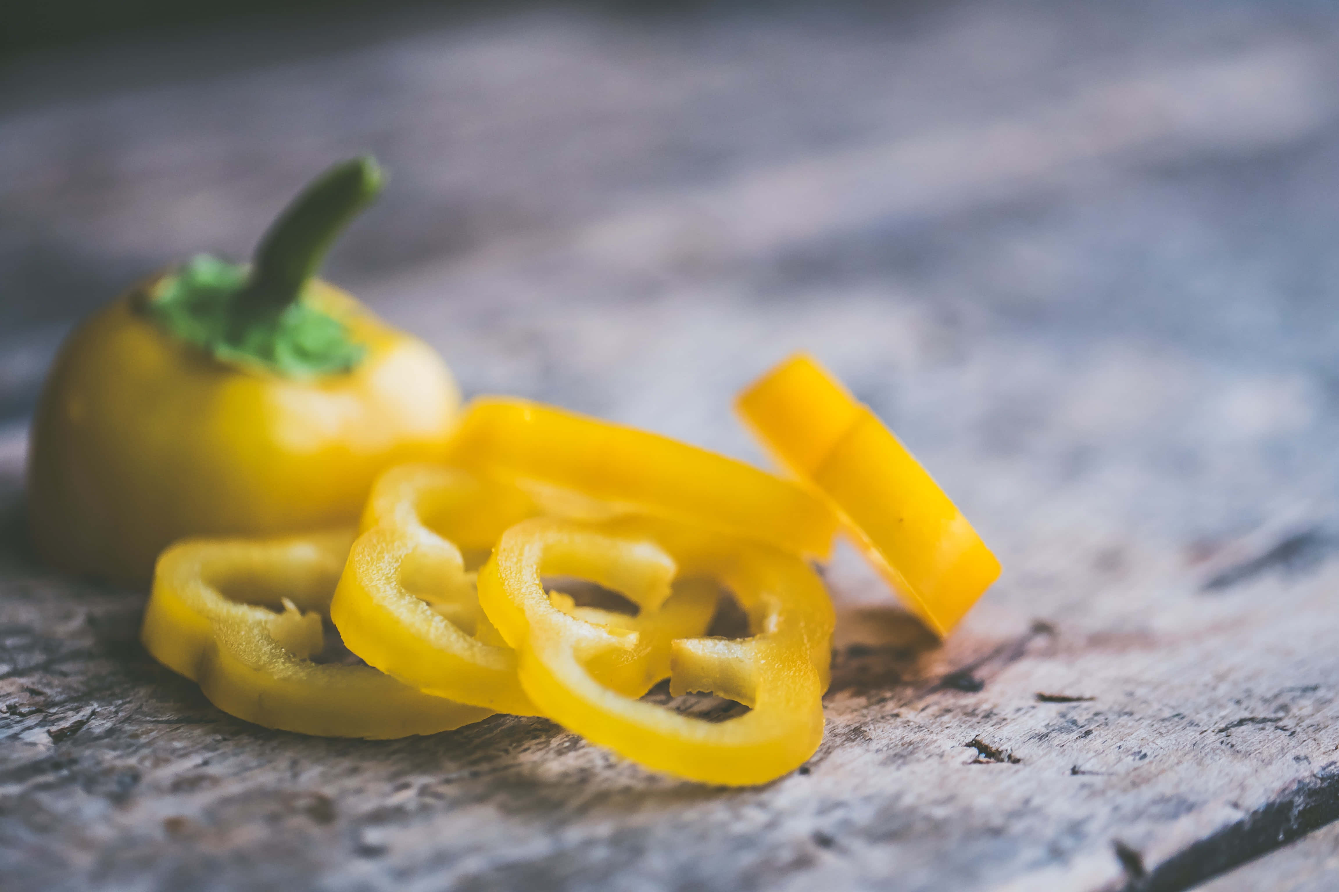 Yellow Bell Pepper 桌布 壁紙 — 切片黃色甜椒圈和整個甜椒放在風化的木質表面上，景深較淺。