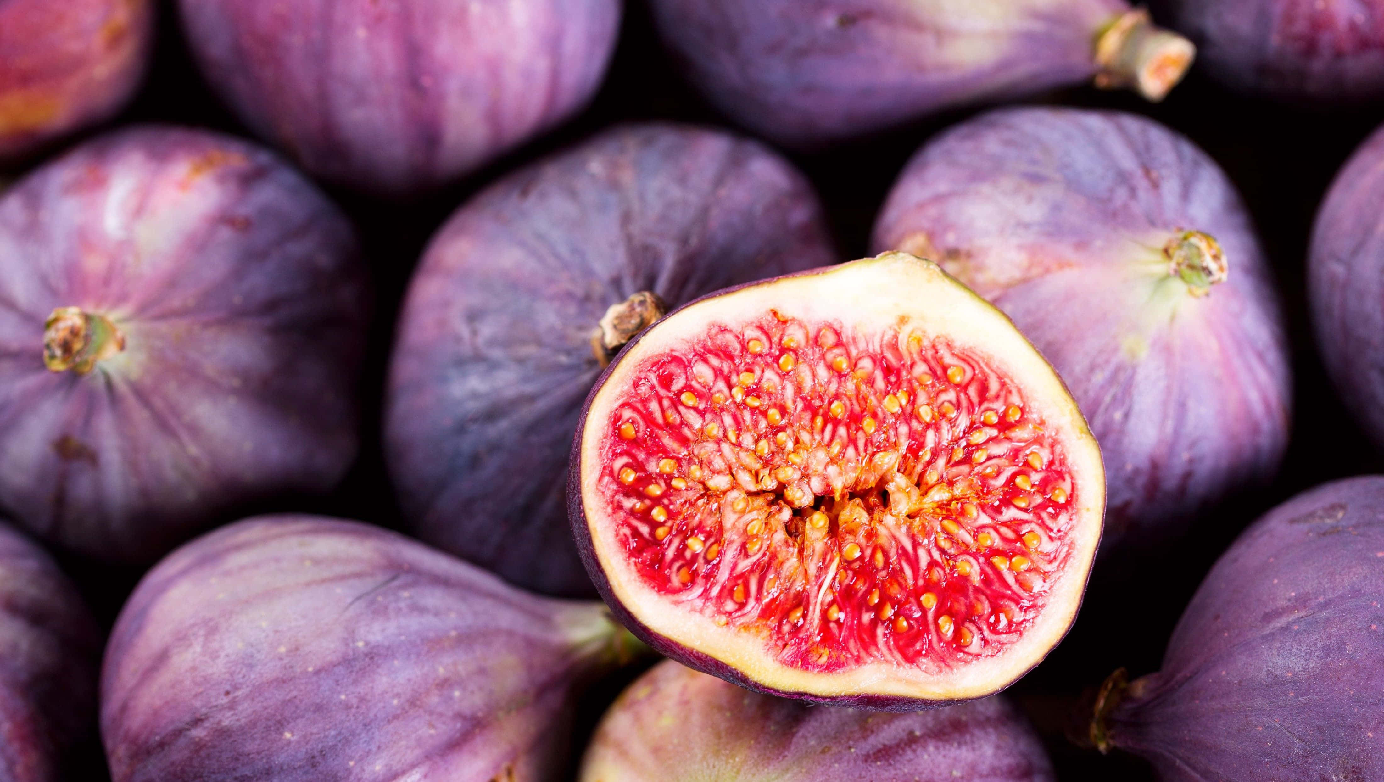 Purple Figs 桌布 壁紙 — 切開嘅紫色無花果特寫，露出多汁嘅粉紅色果肉同金色種子，周圍係成個無花果。