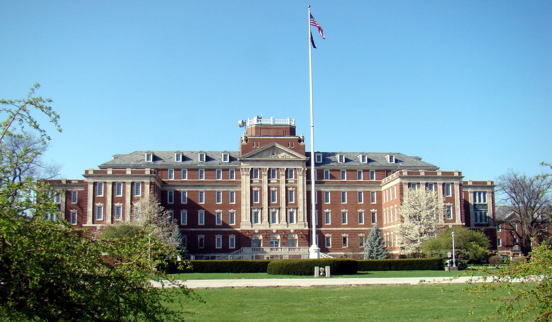 大型大學建築，帶有旗桿和綠色草坪，在陽光明媚的日子裡。