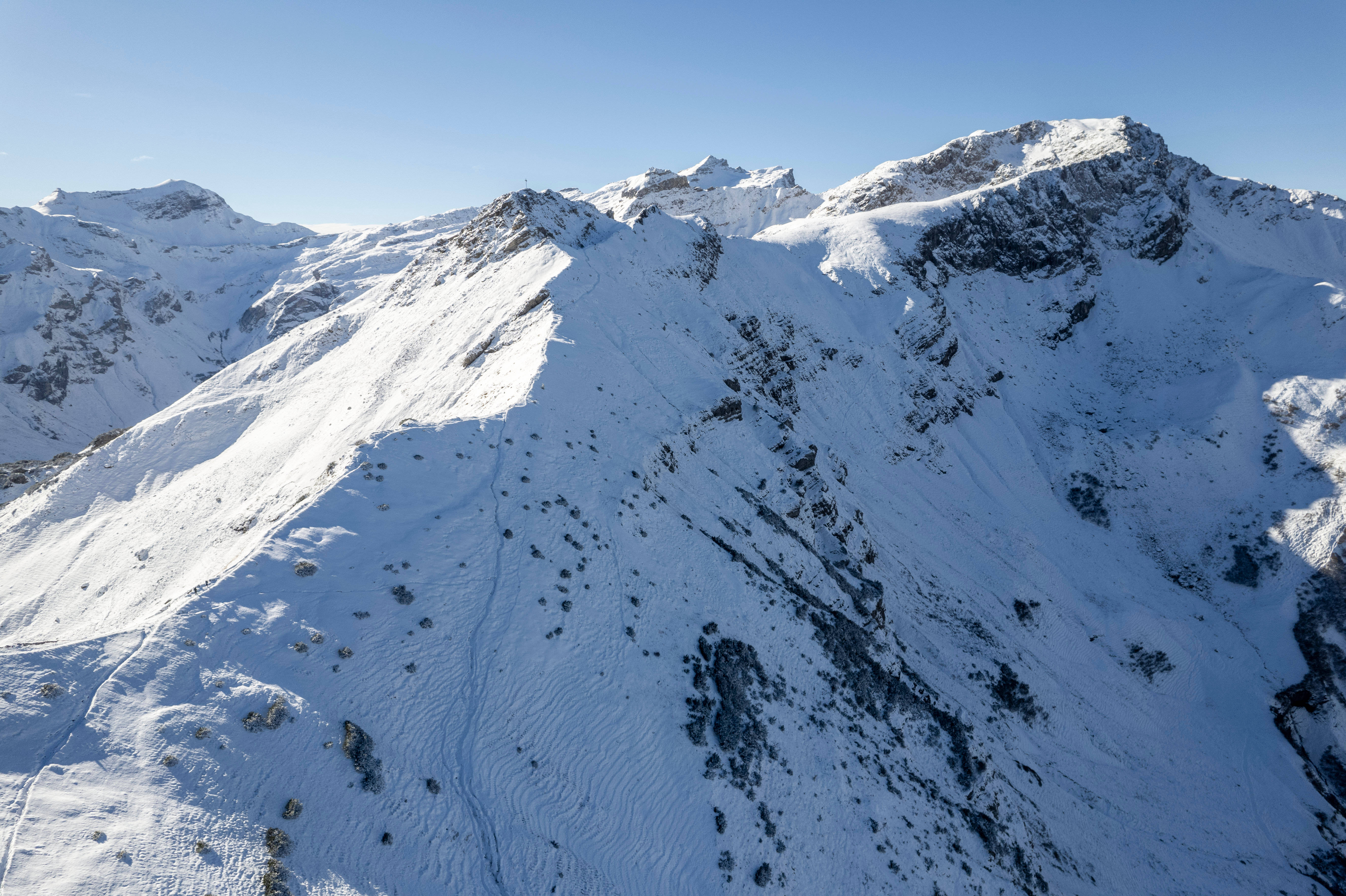 列支敦士登山頂 壁紙 — 從高空俯瞰白雪覆蓋的山峰，在清澈藍天下，有尖銳的岩石山脊和陽光普照的山坡。