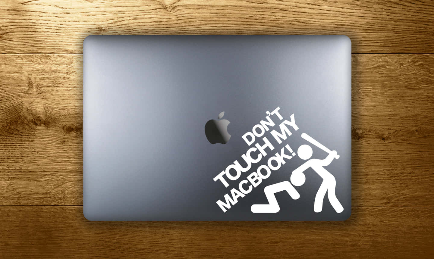 銀色MacBook上貼有「Don't Touch My Macbook!」貼紙的木質桌面。