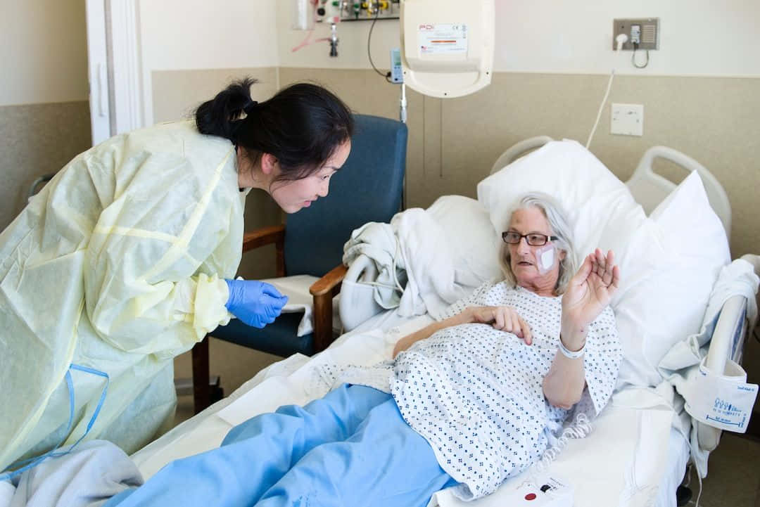 穿著防護裝備的護士正在檢查醫院病床上的老年病人。