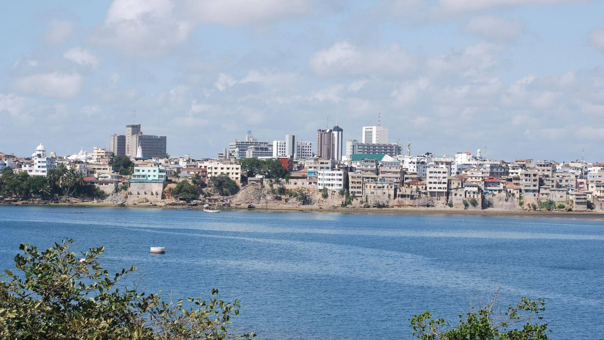 利比里亞河景 壁紙 — 海岸城市景觀，現代與傳統建築沿著平靜的藍色海灣，天空部分多雲。