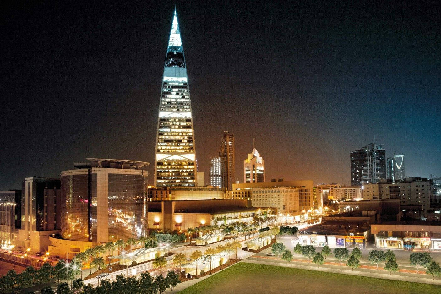 利雅得阿法賽利亞中心夜景 壁紙 — 一座高聳入雲的發光摩天大樓主宰著充滿活力的城市夜景，下方是閃爍的窗戶和棕櫚樹成蔭的街道。