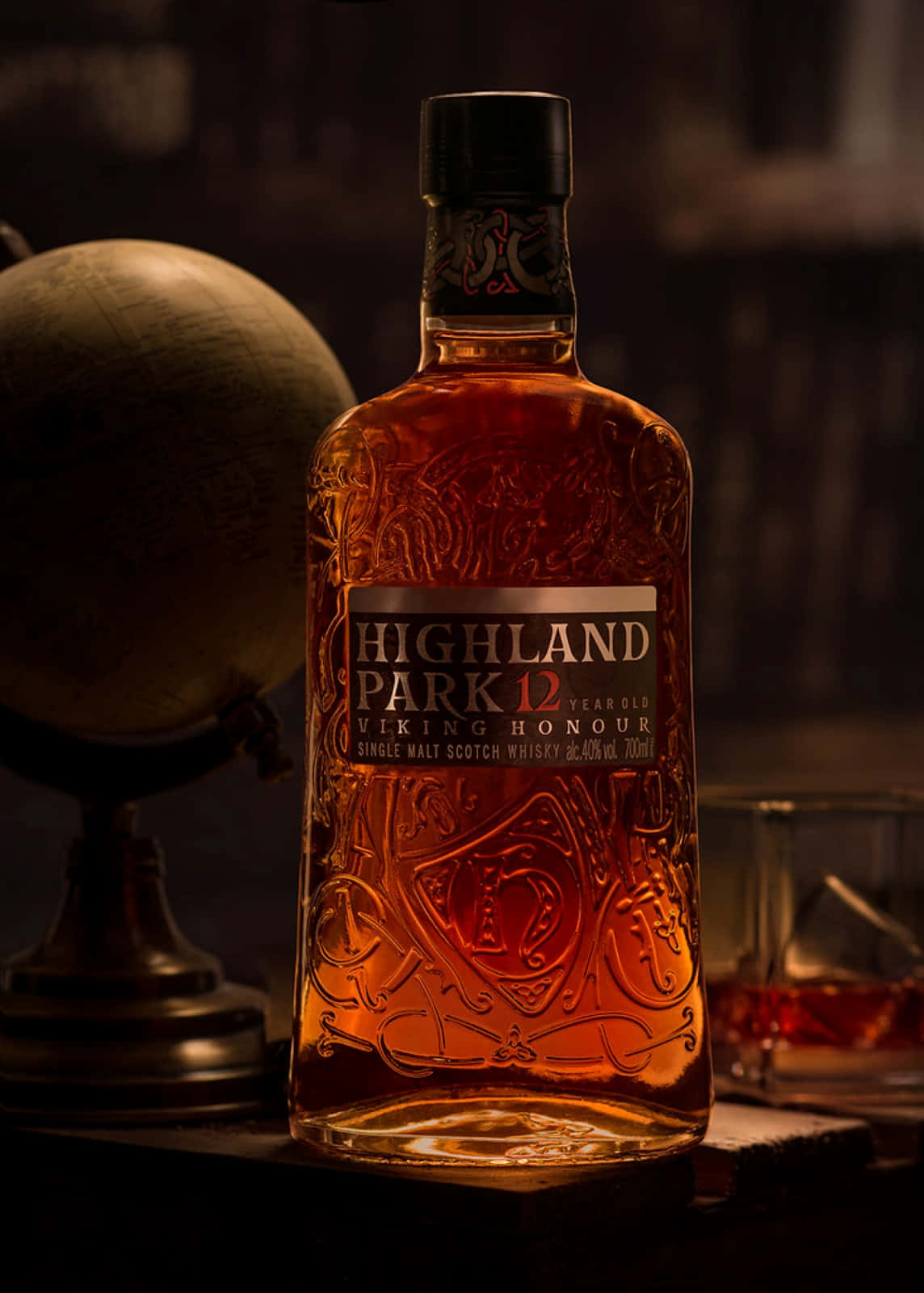 在黑暗環境中，一瓶 Highland Park 威士忌與地球儀和玻璃杯。