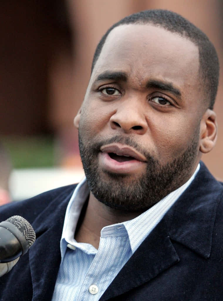 前市長Kwame Kilpatrick發表講話 壁紙 — 一個留鬍鬚的男人喺戶外對住咪高峰講嘢嘅特寫相。