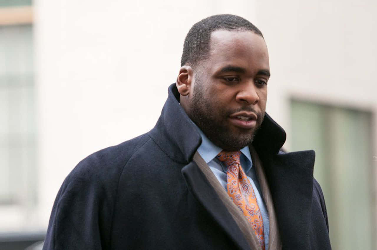 前底特律市長Kwame Kilpatrick 壁紙 — 一個穿著深色外套和圖案領帶的男人，帶著嚴肅的表情在戶外行走。