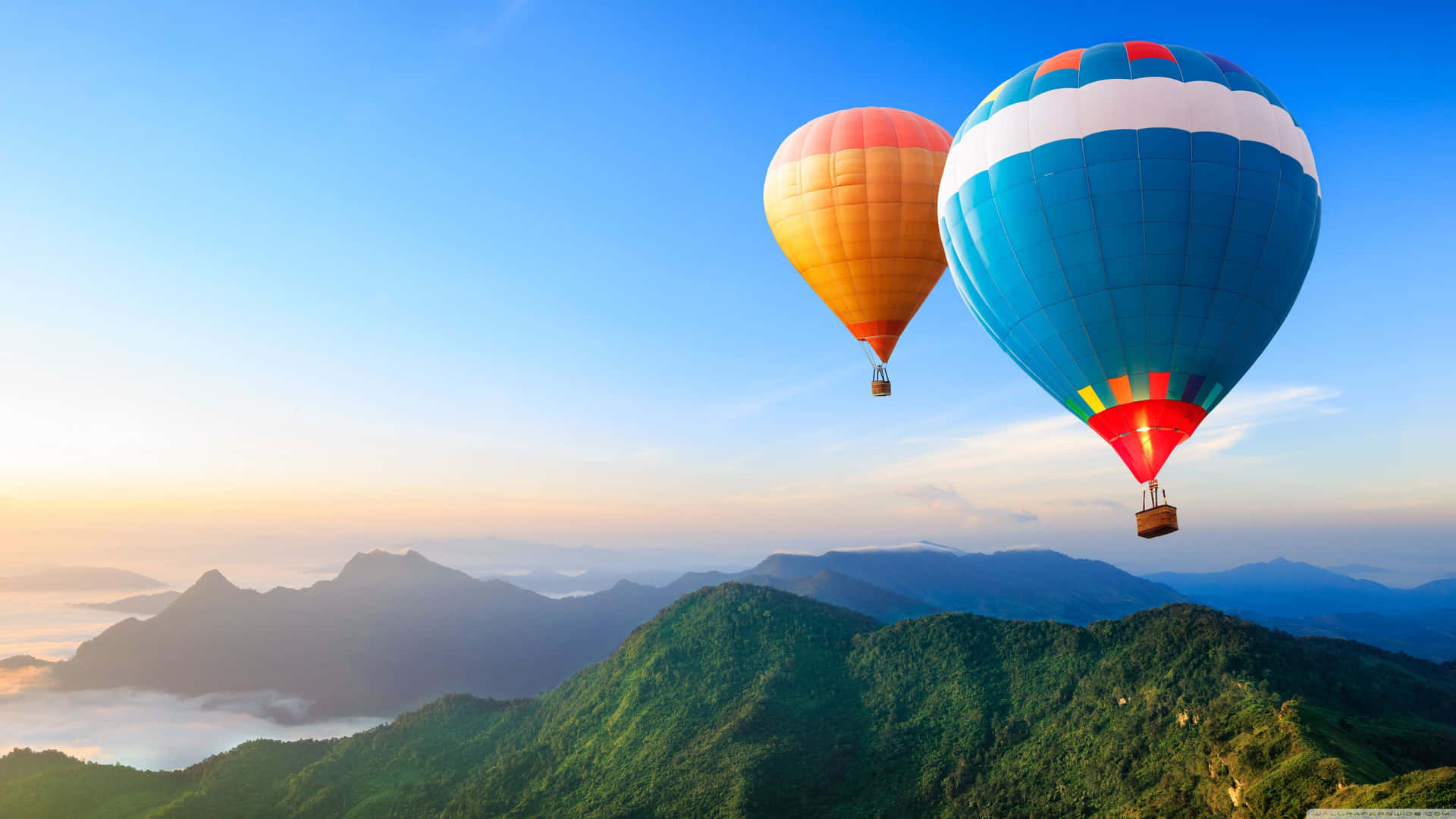 兩個熱氣球在日出時飄浮在山峰之上。