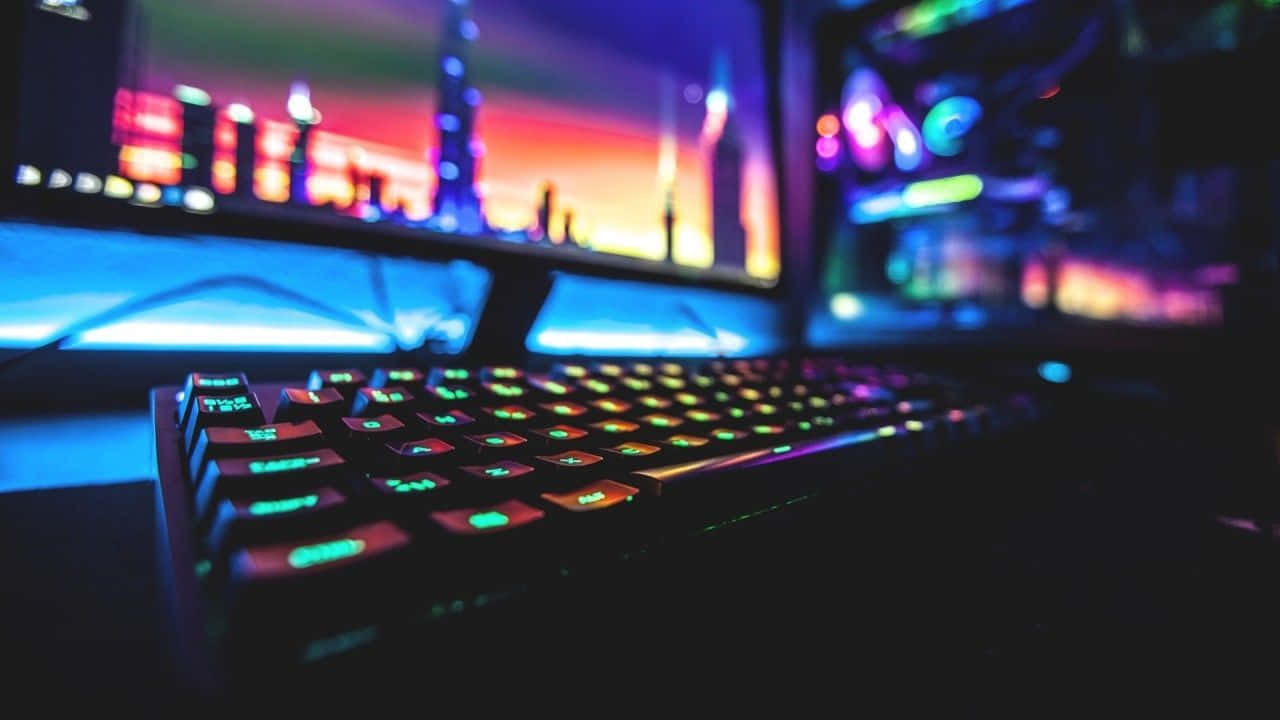 Cool Gaming 桌布 壁紙 — 前景中發光的RGB鍵盤，背後顯示器上模糊的城市天際線呈現鮮豔霓虹色調。