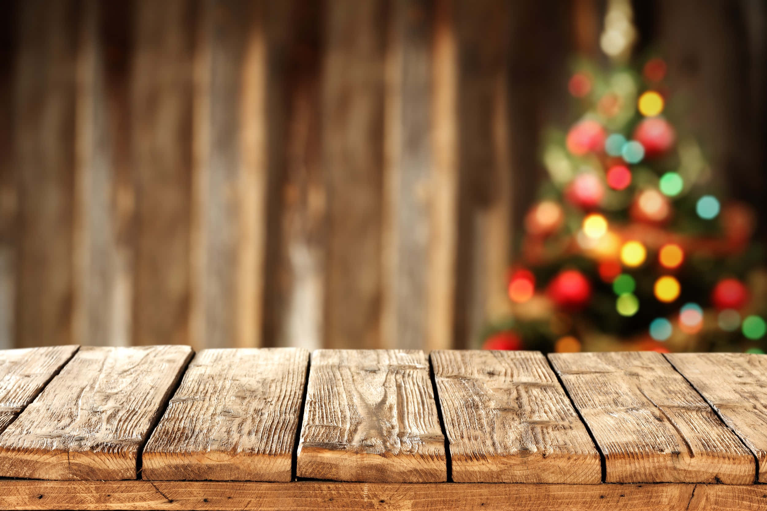 Vintage Christmas 桌布 壁紙 — 前景是風化的木質桌面，背景中模糊的聖誕樹燈光溫暖地閃爍。