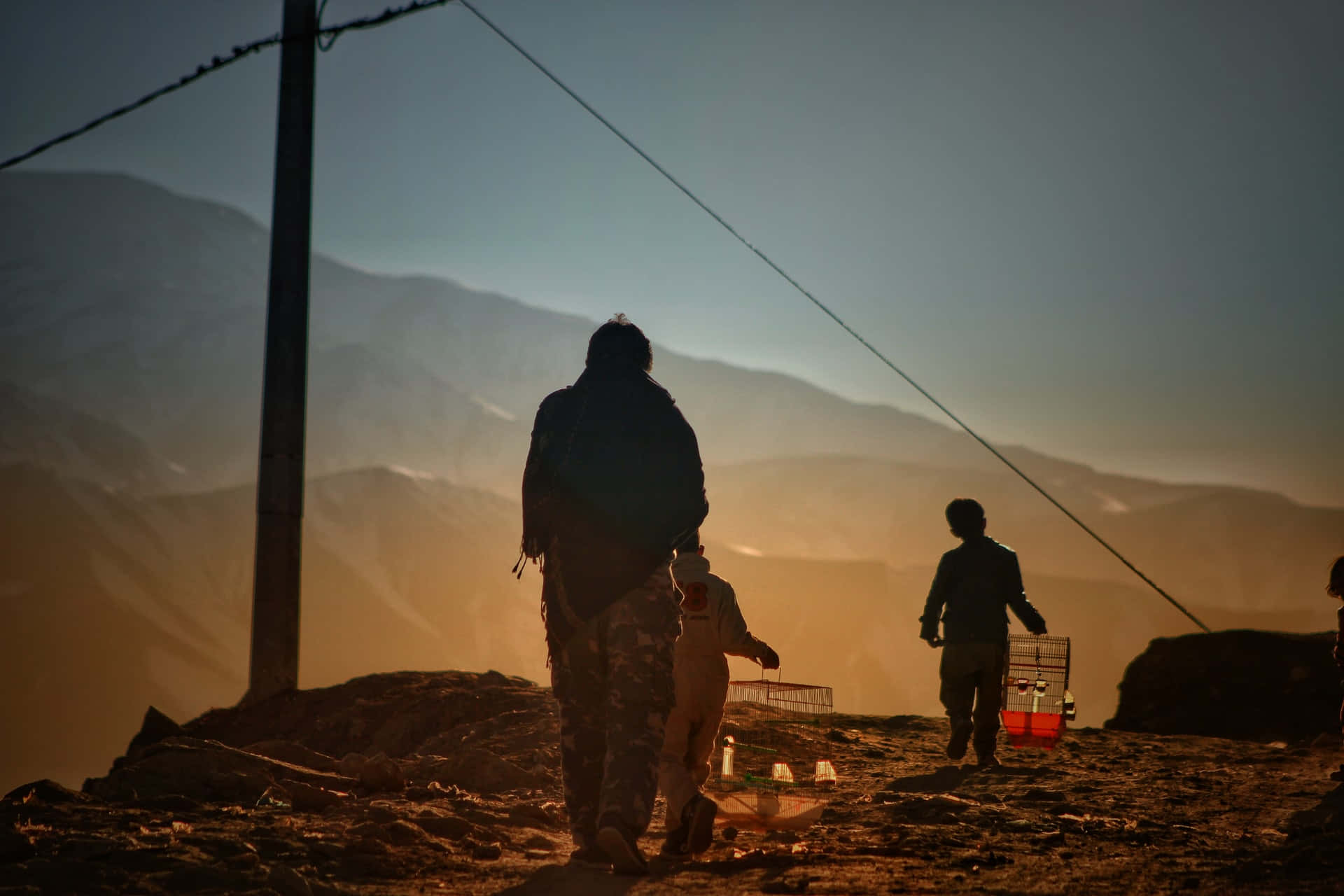 Afghanistan 桌布 壁紙 — 剪影人物在黃金時段走過崎嶇的山脊，遠峰沐浴在溫暖的光線中。