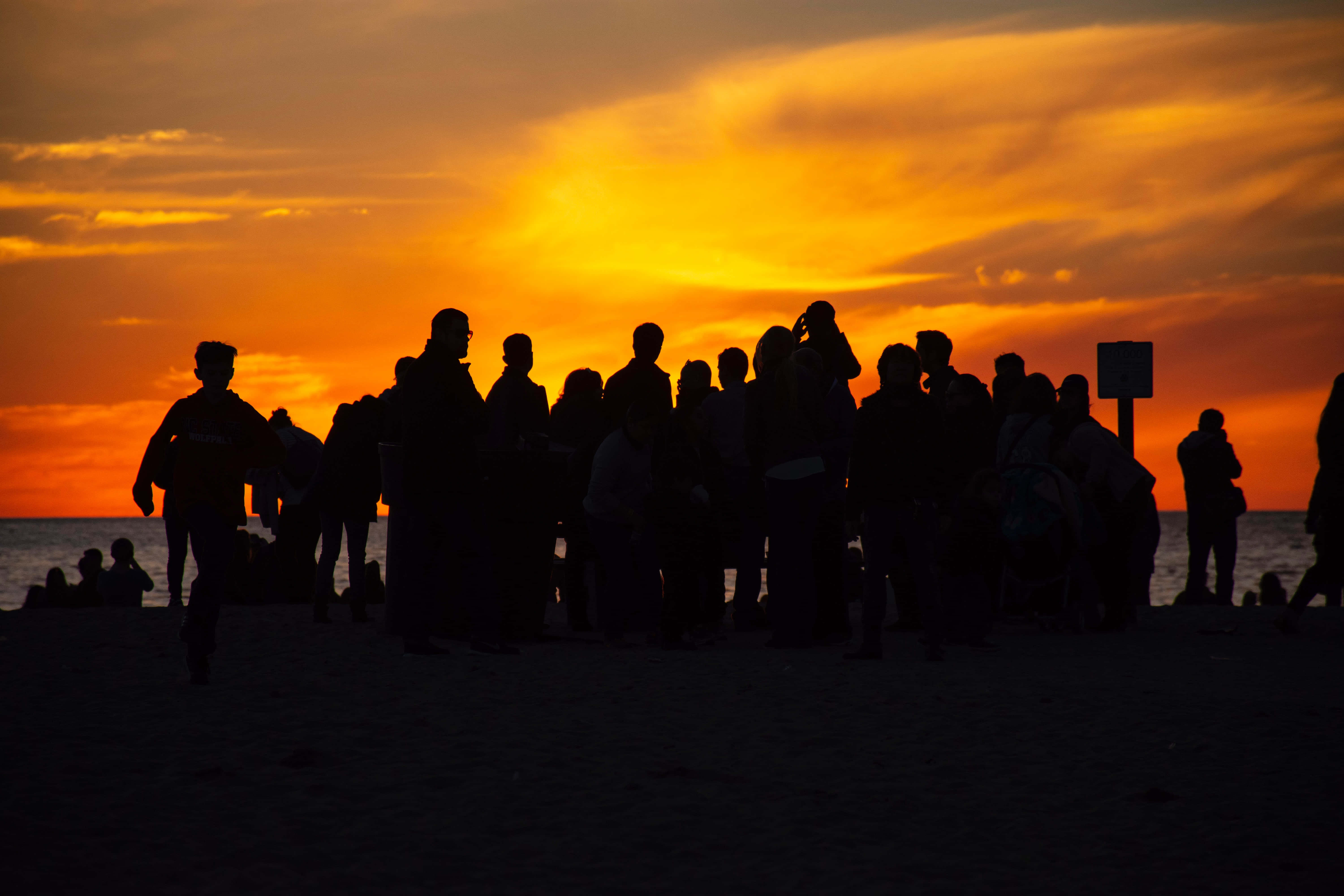 People 桌布 壁紙 — 剪影人群聚集在海灘上，火熱的橙色夕陽染紅了天空和海洋。