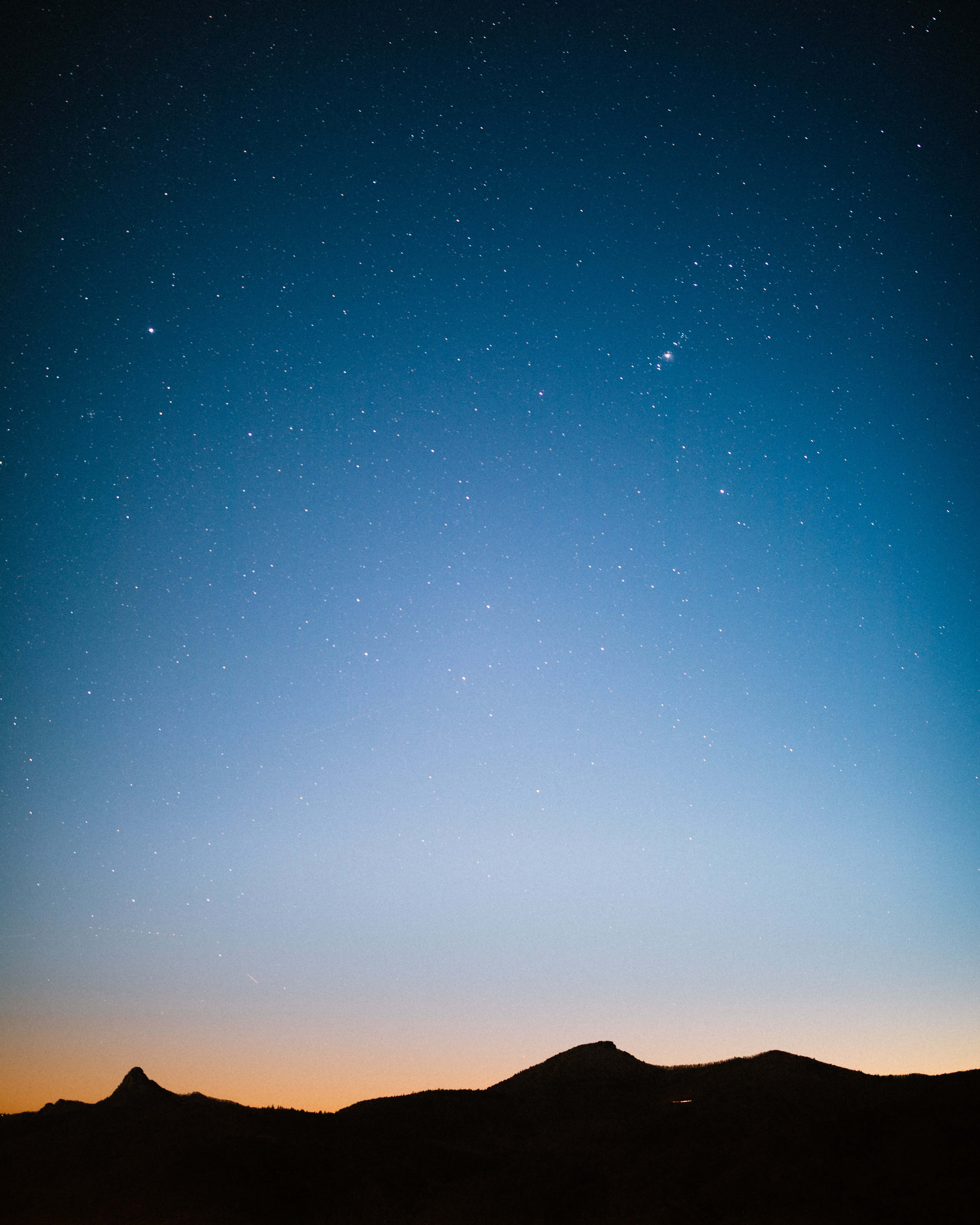 Silhouette 桌布 壁紙 — 剪影山脈仰望繁星點點的暮色天空，散發著漸變藍色和橙色調的光芒。