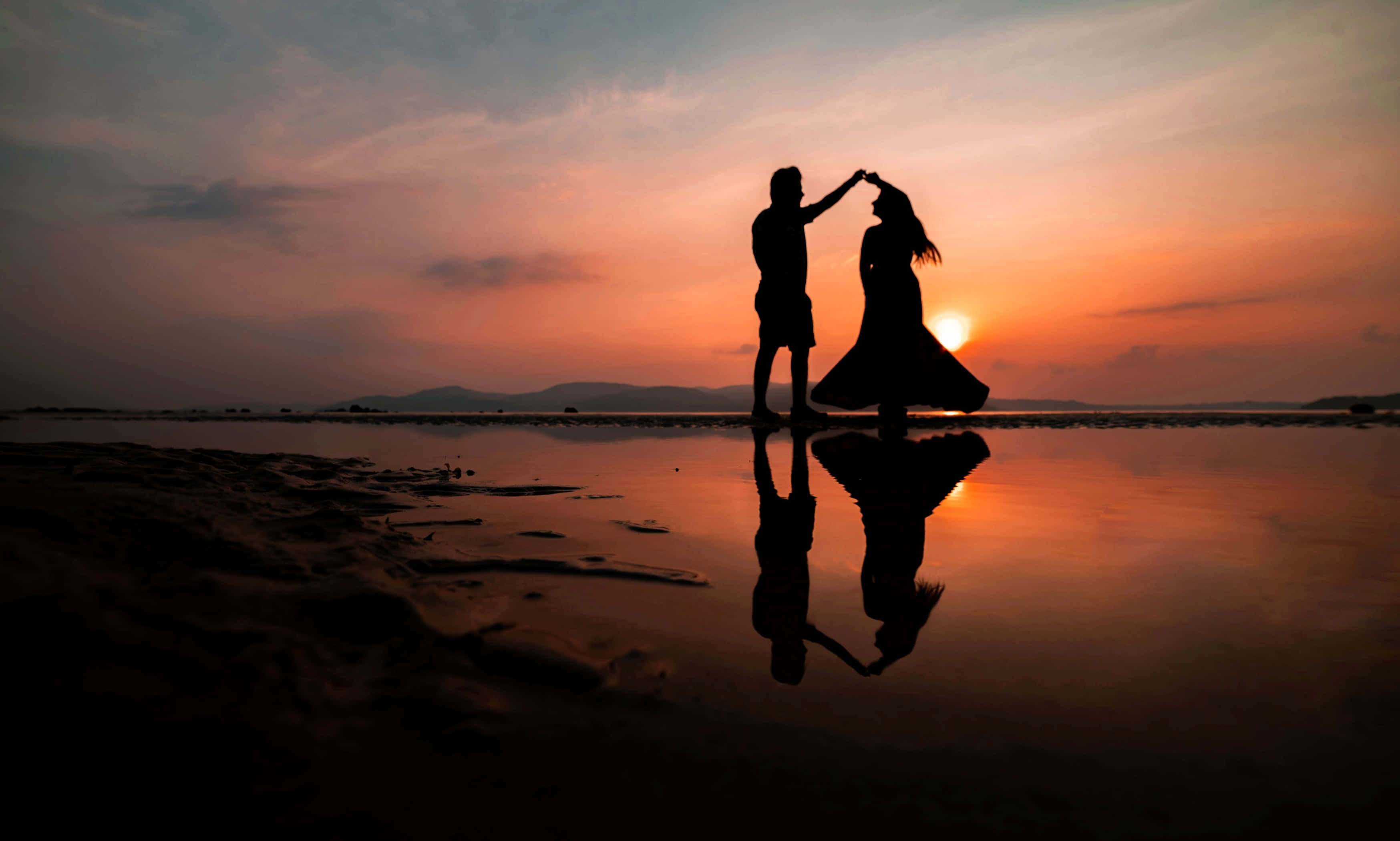 Beach Love 桌布 壁紙 — 剪影情侶在濕沙上跳舞，鮮豔的日落倒映在淺水中，形成完美的鏡像。