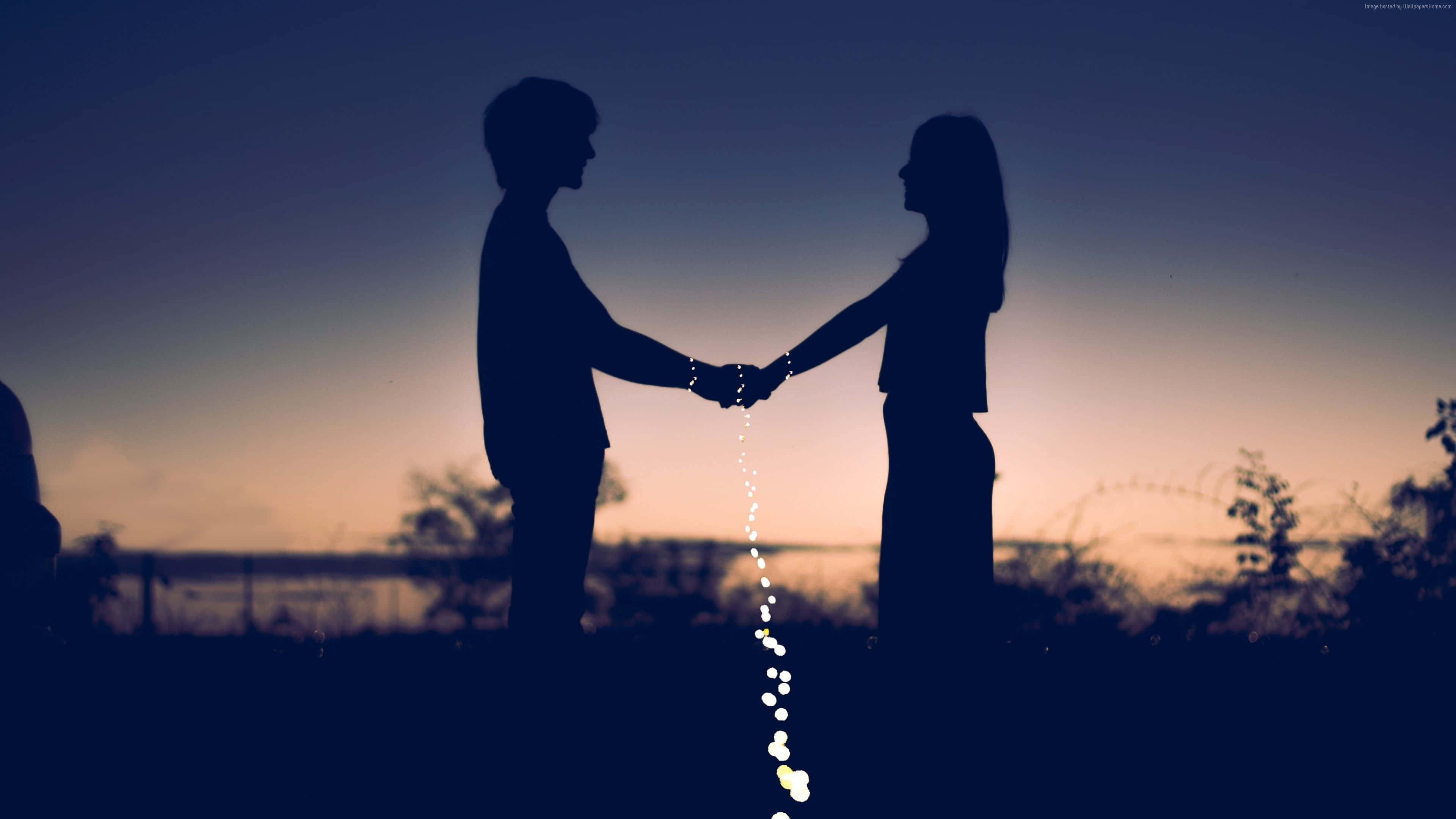 4K Love 桌布 壁紙 — 剪影情侶牽手，發光燈光在他們之間如瀑布般流下，映襯著暮色天空。