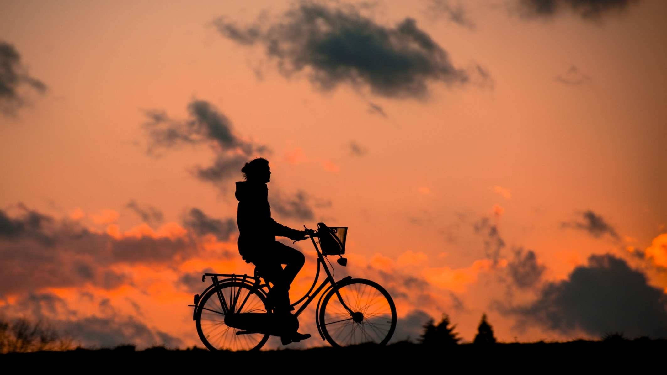剪影男孩騎自行車 壁紙 — 一個人騎著單車的剪影，背景是火紅的橙色日落天空，散落著雲朵。