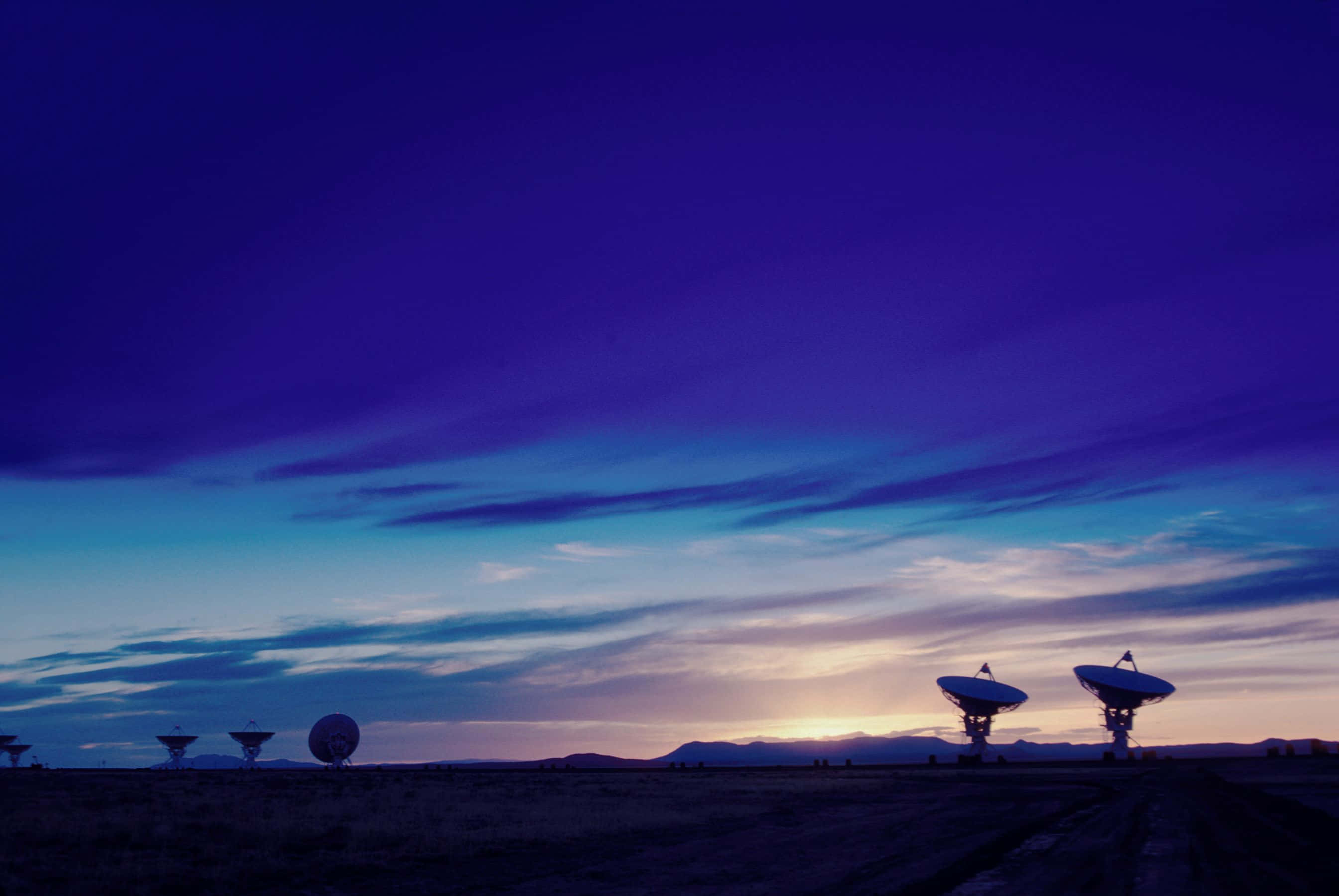 Radio Telescope 桌布 壁紙 — 剪影的無線電望遠鏡矗立在廣闊的沙漠中，在暮色下呈現漸變的紫色和藍色天空。