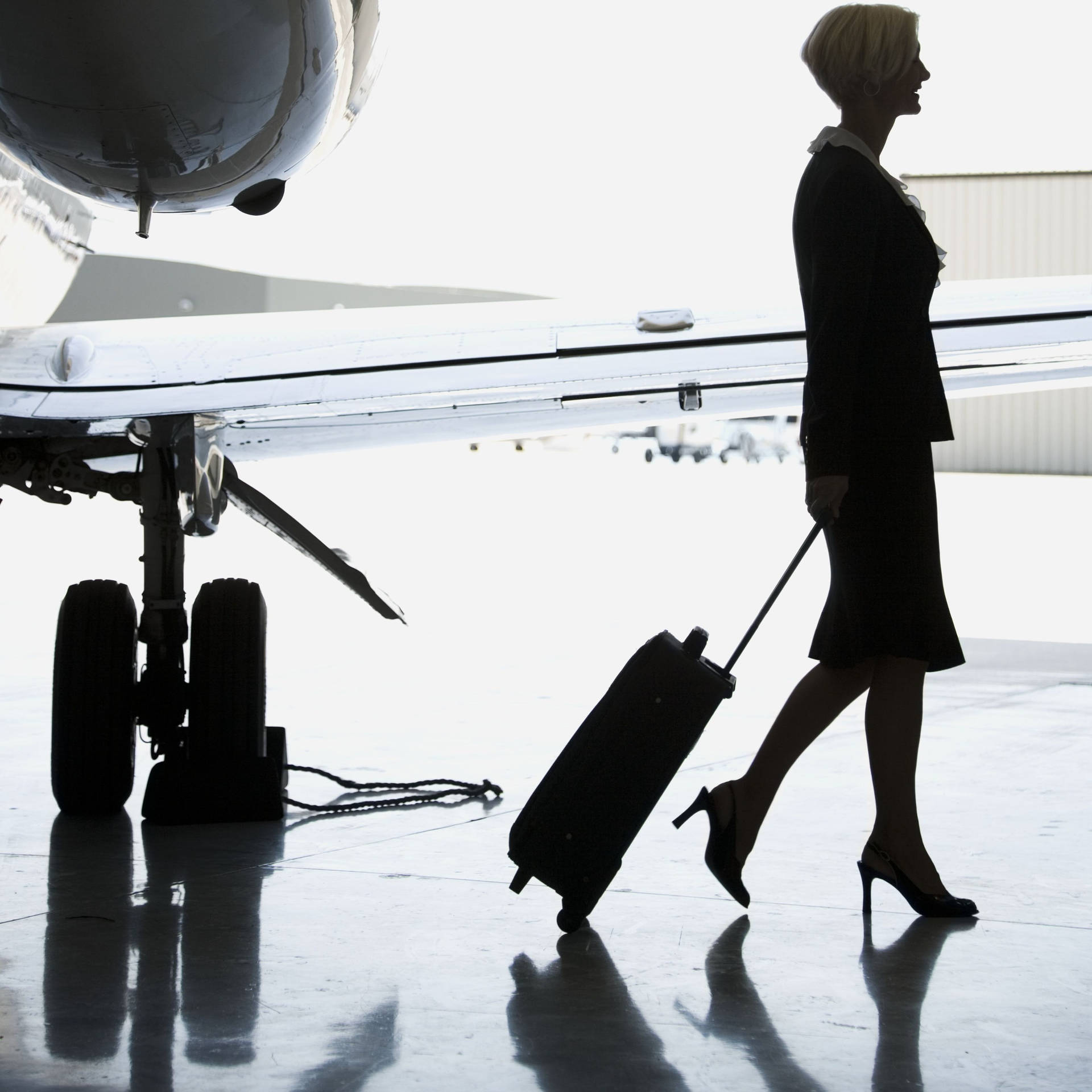 商務女性在停機坪上拉著行李箱走在飛機旁邊。