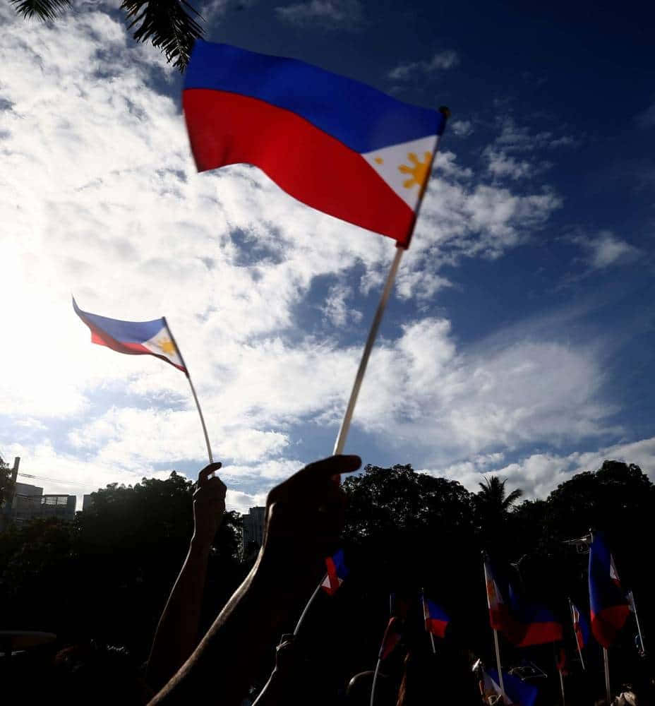 Philippines 桌布 壁紙 — 剪影般的手在明亮的陰天天空下揮舞菲律賓國旗，這是一場白天的聚會。