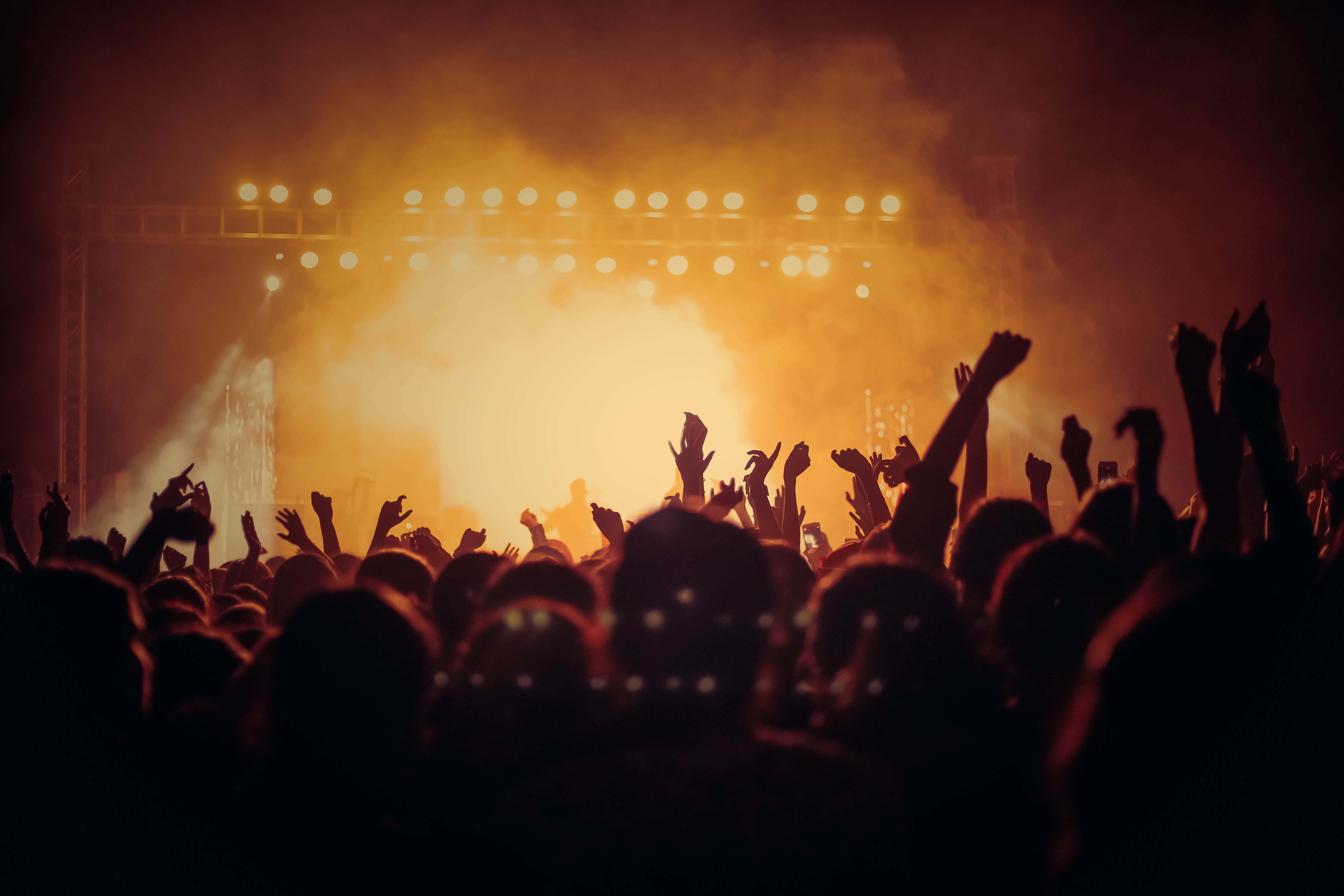 music festival 桌布 壁紙 — 剪影般的演唱會人群在煙霧瀰漫中向發光的舞台燈光舉起雙手。