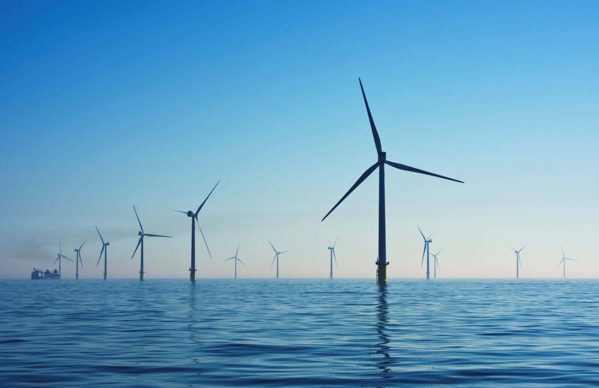 Renewable Energy 桌布 壁紙 — 剪影般的離岸風力發電機在平靜的藍色海水中矗立，天空呈現清晰的漸變色。